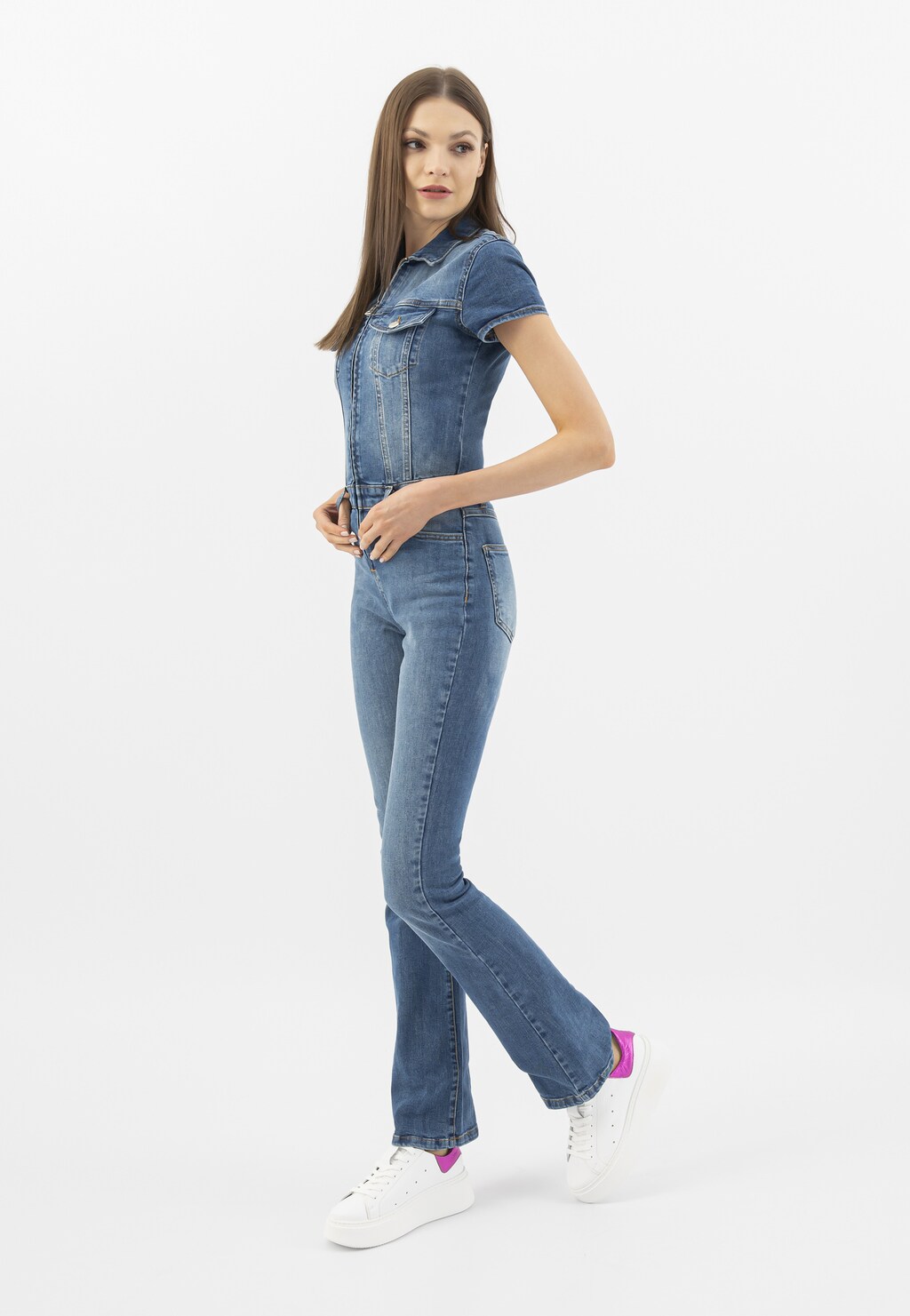 Modelka w jeansowym kombinezonie prezentuje białe trampki Wojas model 46285-75 z charakterystycznymi różowymi metalicznymi wstawkami, idealnie uzupełniające casualowy look.