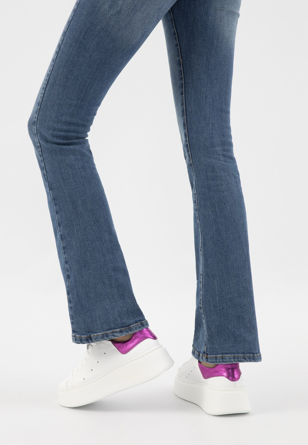 Białe trampki Wojas model 46285-75 z metaliczną różową wstawką na pięcie, noszone z jeansami typu dzwony. Widok z tyłu na nogi osoby w ruchu.