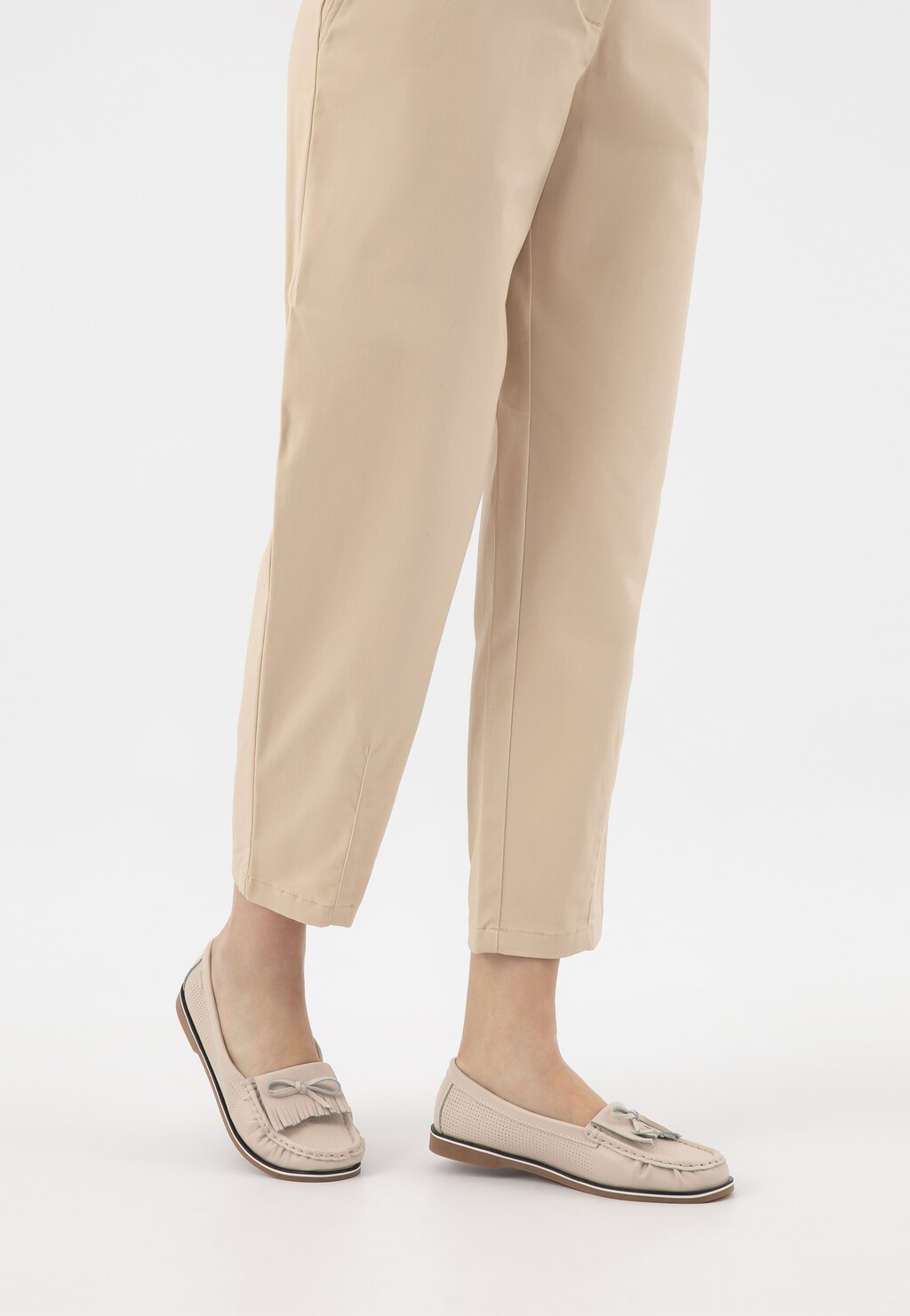 Beżowe mokasyny damskie Wojas 46293-55 z ażurowaną cholewką i ozdobną kokardką, noszone do jasnych spodni, widoczne z boku w całej stylizacji.