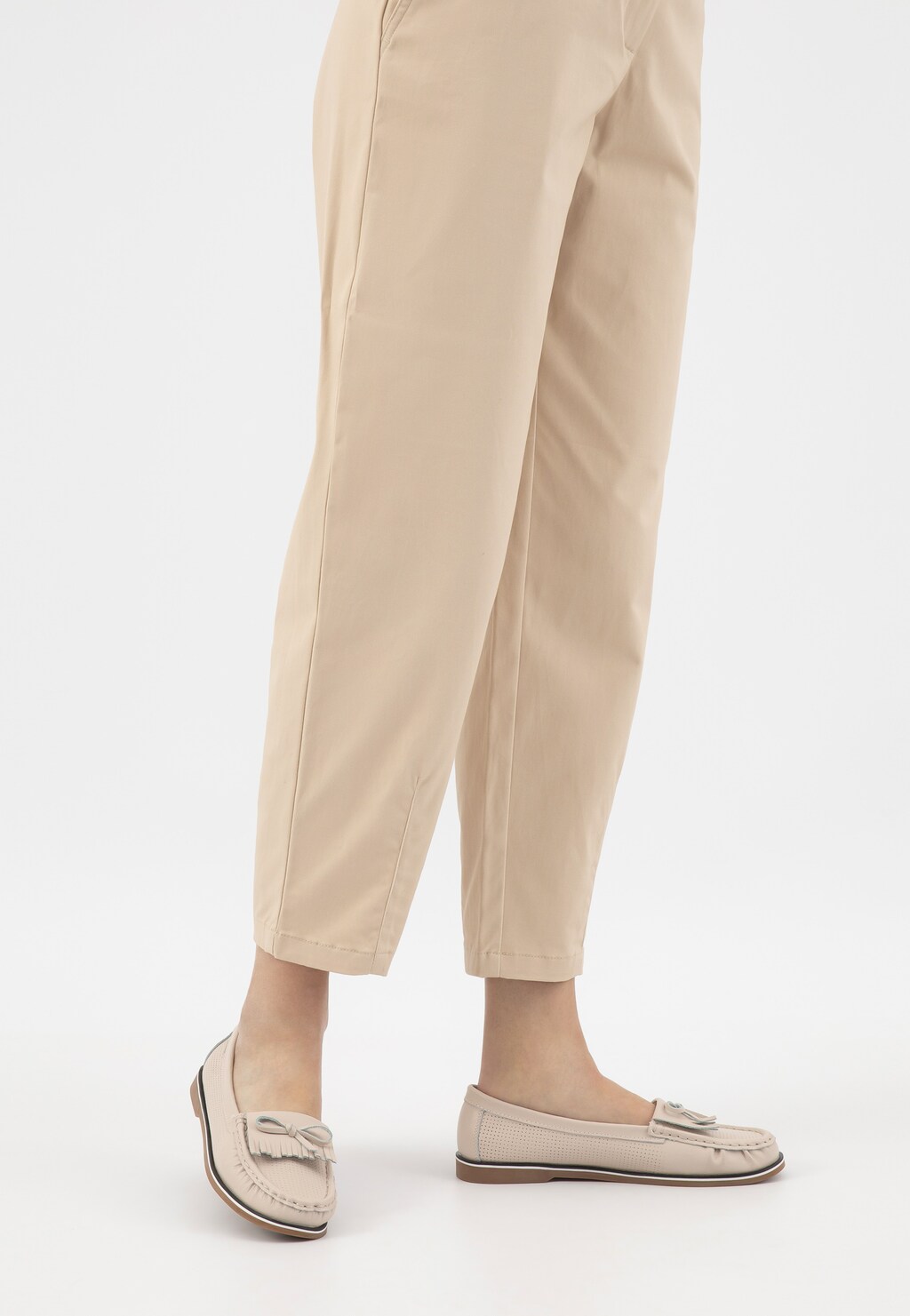 Beżowe damskie mokasyny Wojas model 46293-55 z ażurowaną cholewką i ozdobną kokardką, prezentowane na nogach osoby w jasnych spodniach.