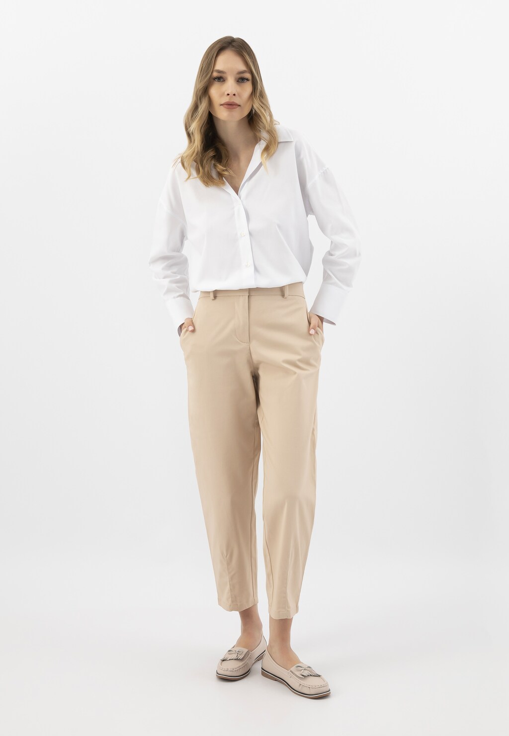 Modelka w eleganckiej stylizacji z białą koszulą i beżowymi spodniami, prezentująca beżowe mokasyny damskie Wojas z ażurowaną cholewką model 46293-55.