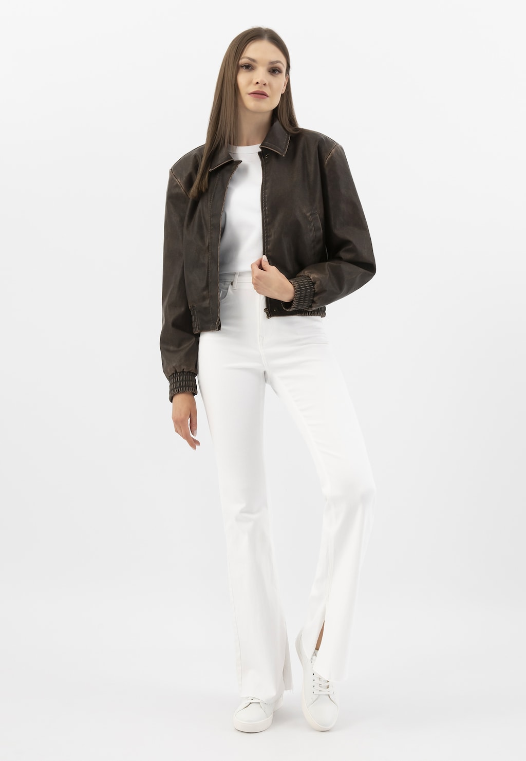 Modelka w białym stroju i brązowej kurtce prezentuje białe trampki damskie Wojas ze skóry licowej model 46019-59, idealne do codziennych stylizacji.