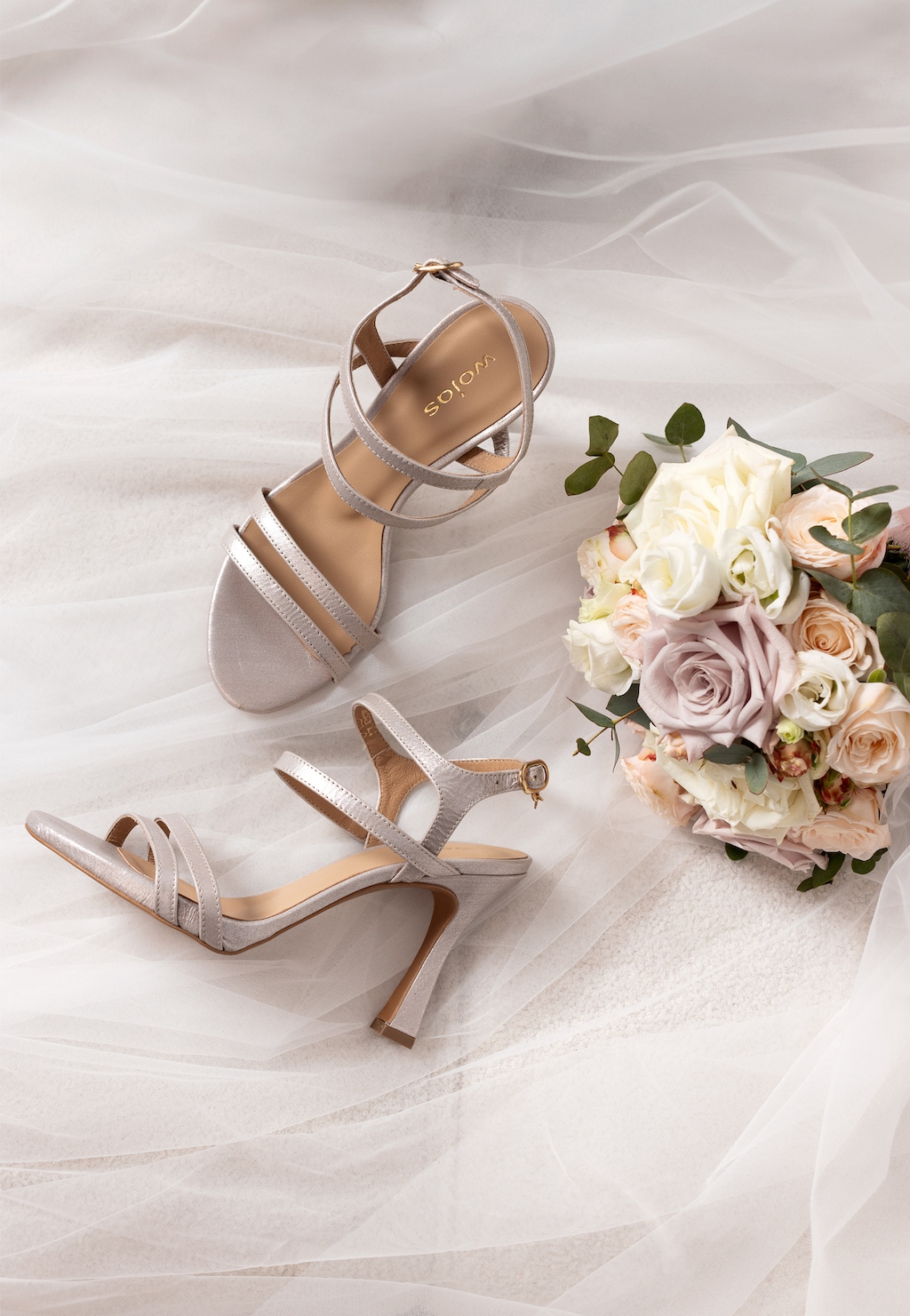 Srebrne sandały Wojas model 76190-59 z weluru foliowanego na szpilce, elegancko ułożone obok bukietu pastelowych róż na delikatnym białym materiale.