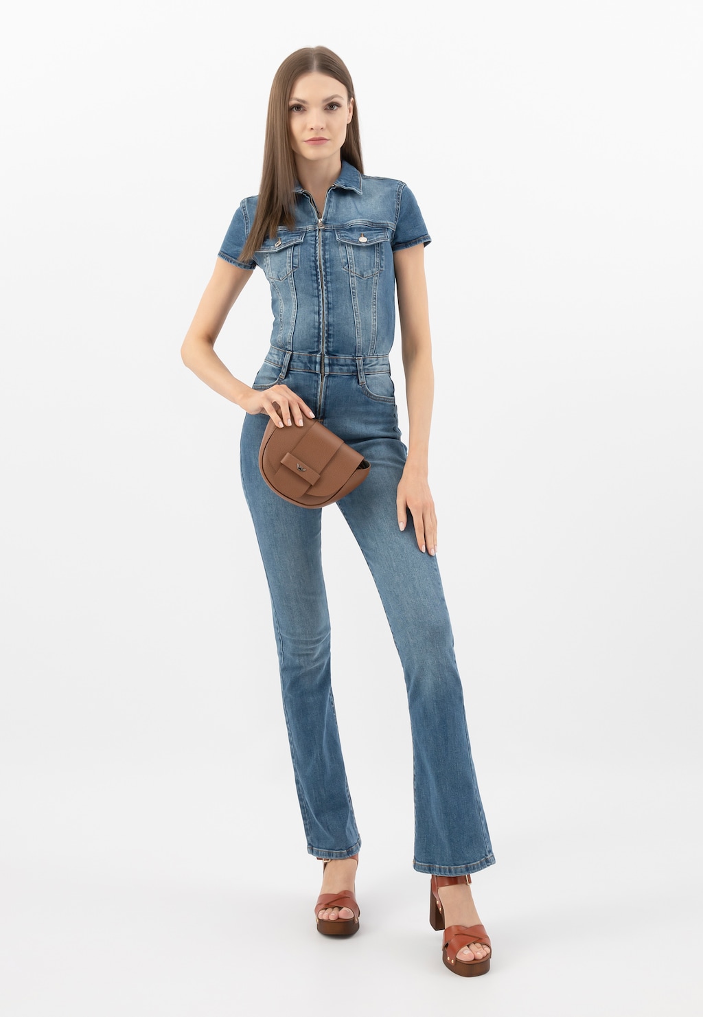 Modelka w jeansowym kombinezonie prezentuje jasnobrązową skórzaną torebkę damską Wojas typu saddle bag model 9816-53, noszoną na ramieniu. Na nogach ma brązowe sandały.