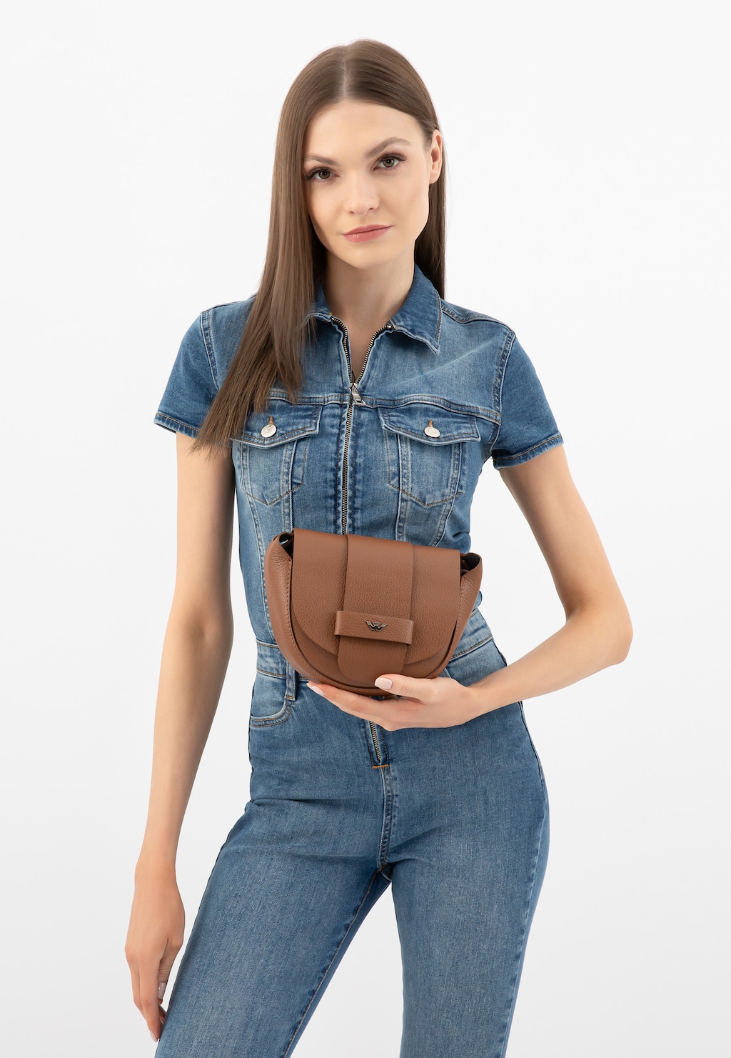 Modelka w jeansowym kombinezonie prezentuje jasnobrązową skórzaną torebkę damską Wojas typu saddle bag model 9816-53 o eleganckim designie z charakterystycznym zapięciem.