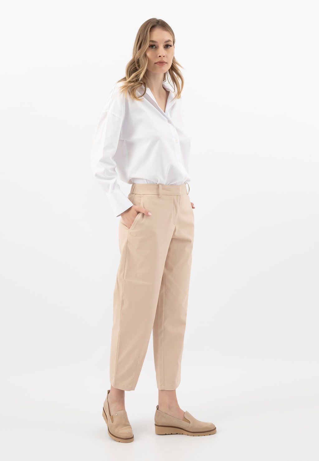 Modelka w eleganckim stroju biznesowym - biała koszula i beżowe spodnie - prezentuje beżowe loafersy damskie Wojas na klinie model 46008-74 w ujęciu całej sylwetki.