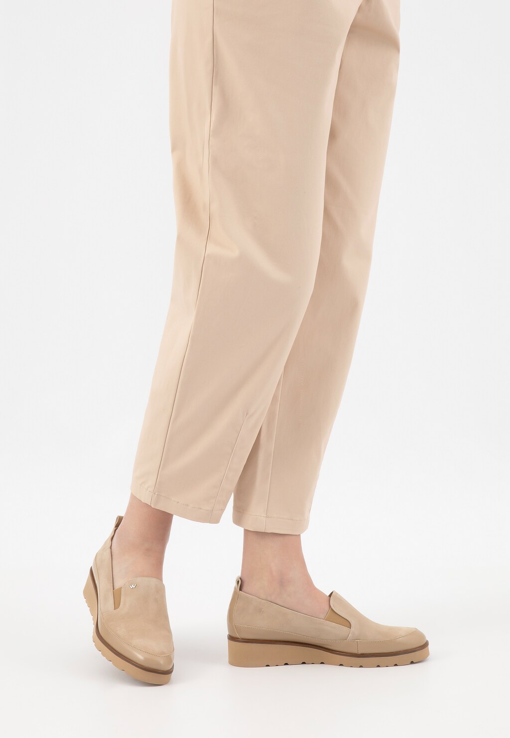 Beżowe loafersy damskie Wojas 46008-74 na klinie, noszone ze spodniami w kremowym kolorze. Widok z boku pokazuje elegancką sylwetkę buta na niewysokiej platformie.