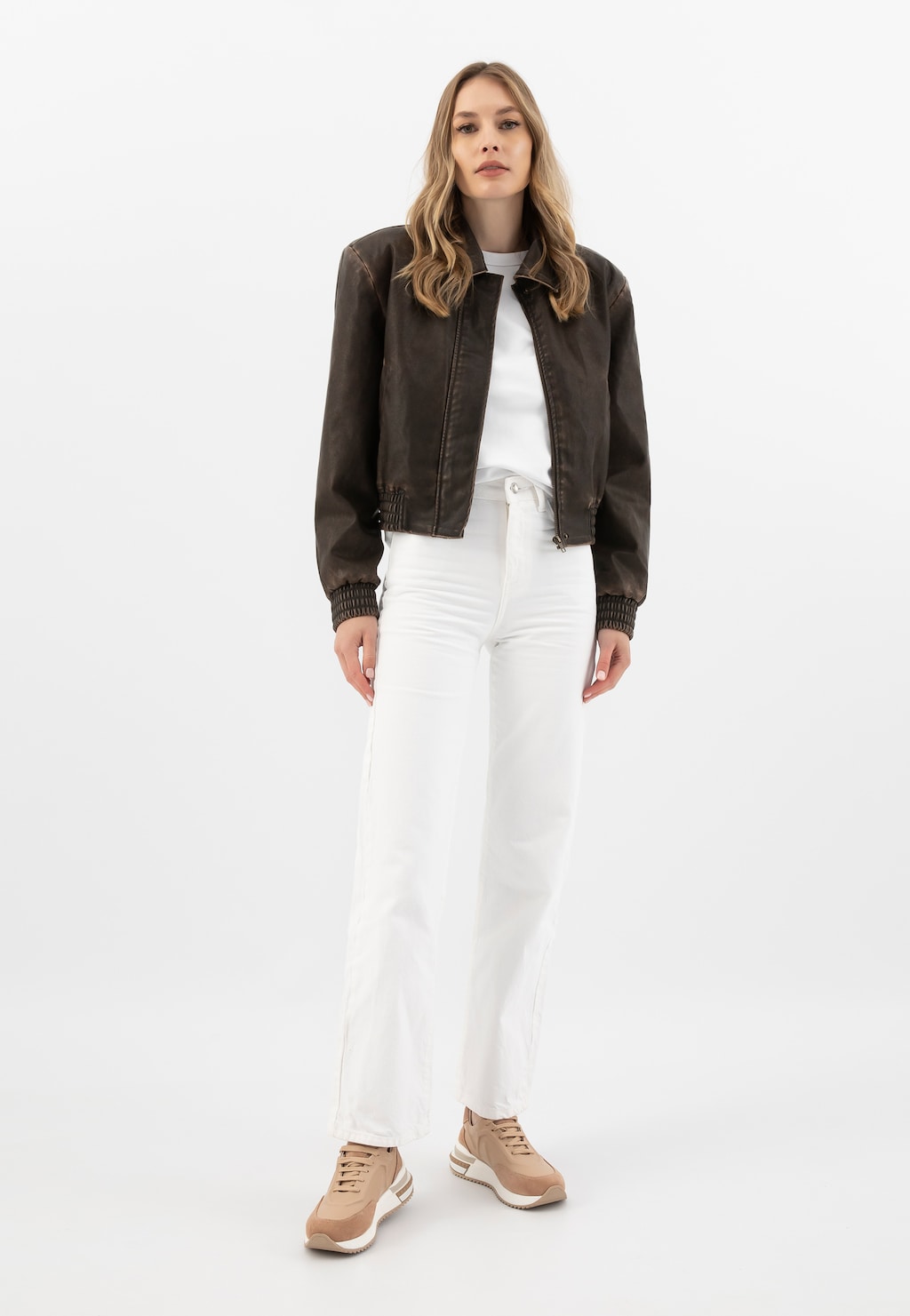 Modelka w brązowej kurtce i białym stroju prezentująca beżowe sneakersy Wojas model 46287-74, wykonane z łączonych skór, widoczne w stylizacji z jasnymi spodniami.