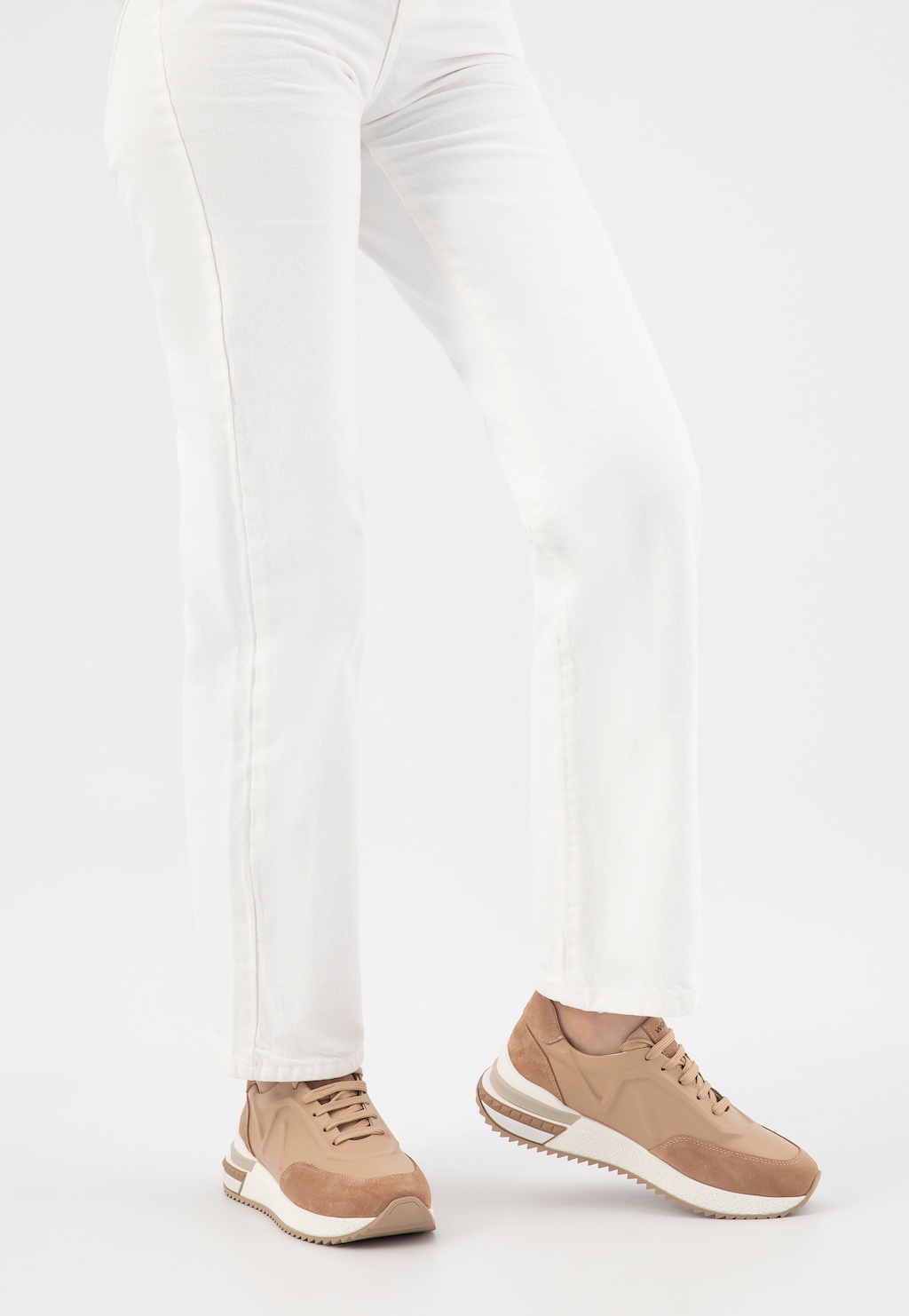 Beżowe sneakersy Wojas 46287-74 noszone z białymi spodniami. Buty damskie z łączonych skór widoczne z profilu, wyposażone w białą podeszwę z brązowym spodem.