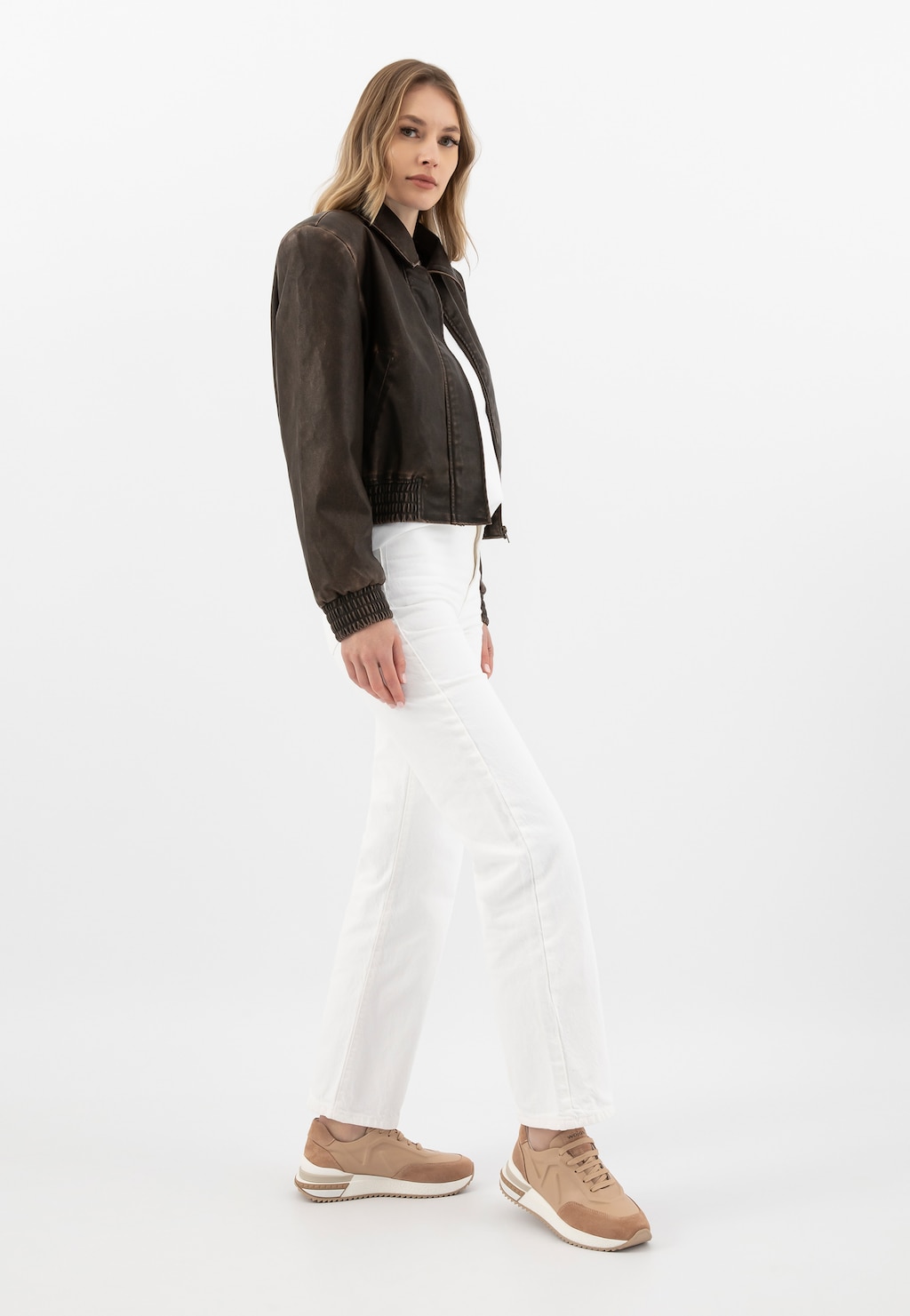 Model w eleganckiej stylizacji z brązową kurtką i białymi spodniami, prezentujący beżowe sneakersy Wojas model 46287-74 wykonane z łączonych skór.