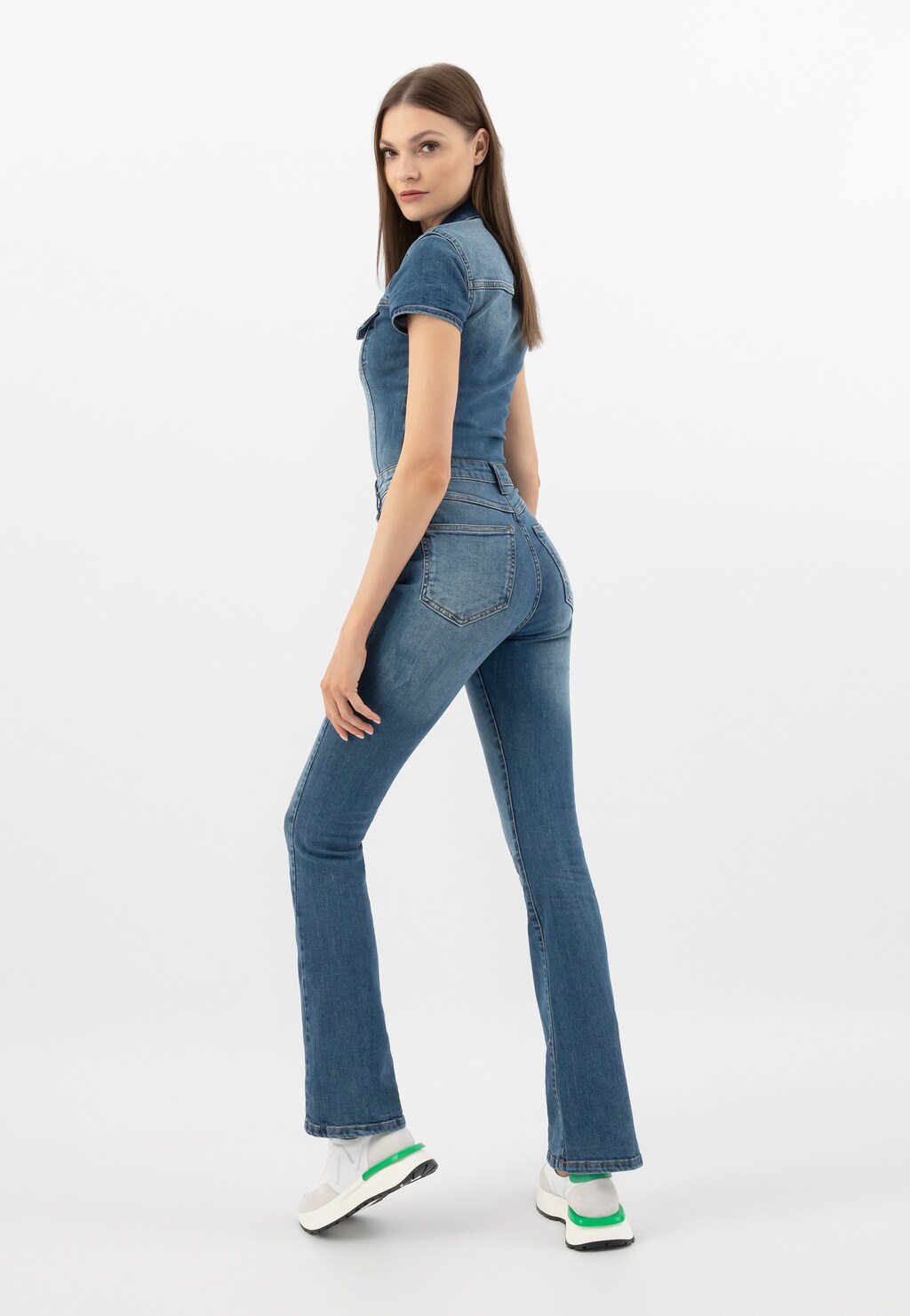 Modelka w jeansowym kombinezonie prezentuje białe sneakersy Wojas model 46288-79 z charakterystycznymi zielonymi akcentami. Buty elegancko uzupełniają casualowy strój.