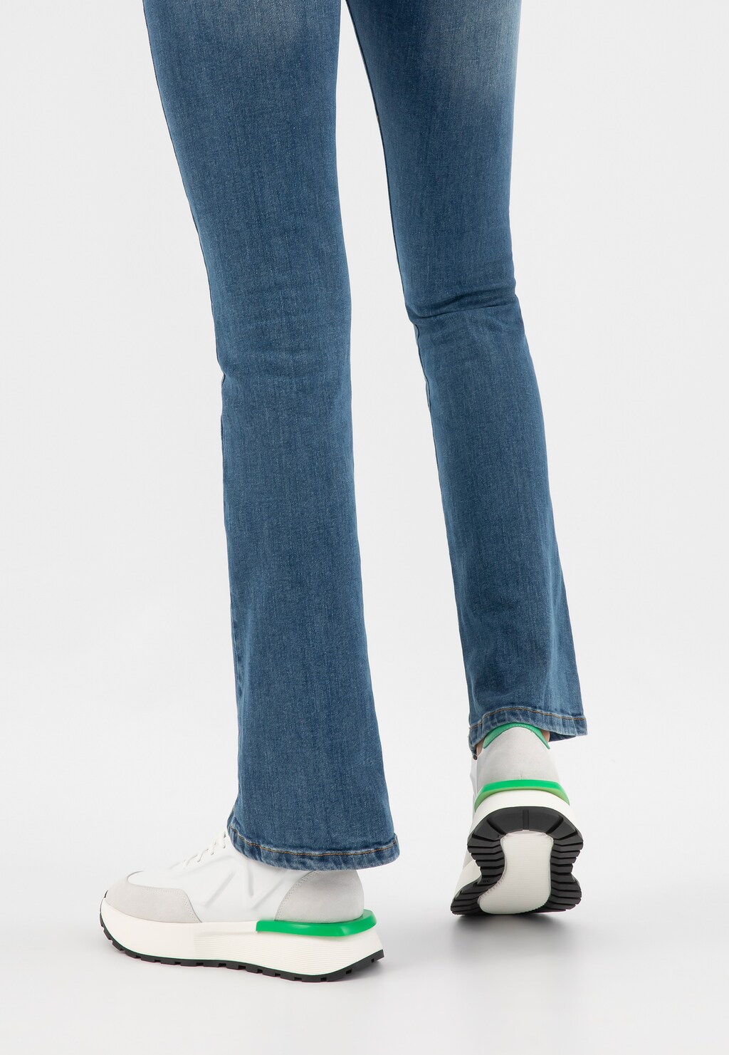 Nogi w niebieskich jeansach i białe sneakersy damskie Wojas model 46288-79 z charakterystycznymi zielonymi akcentami, widok z tyłu pokazujący podeszwę buta.