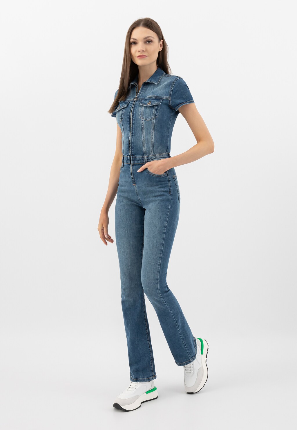 Modelka w jeansowym kombinezonie prezentuje białe sneakersy damskie Wojas model 46288-79 z charakterystycznymi zielonymi akcentami, idealne do casualowych stylizacji.