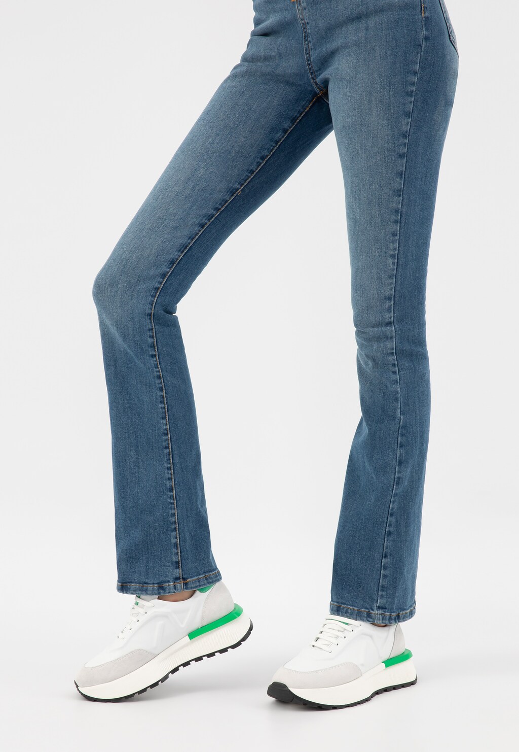 Nogi w niebieskich jeansach typu bootcut i białe sneakersy Wojas model 46288-79 z charakterystycznymi zielonymi akcentami na pięcie i szarymi wstawkami z przodu.