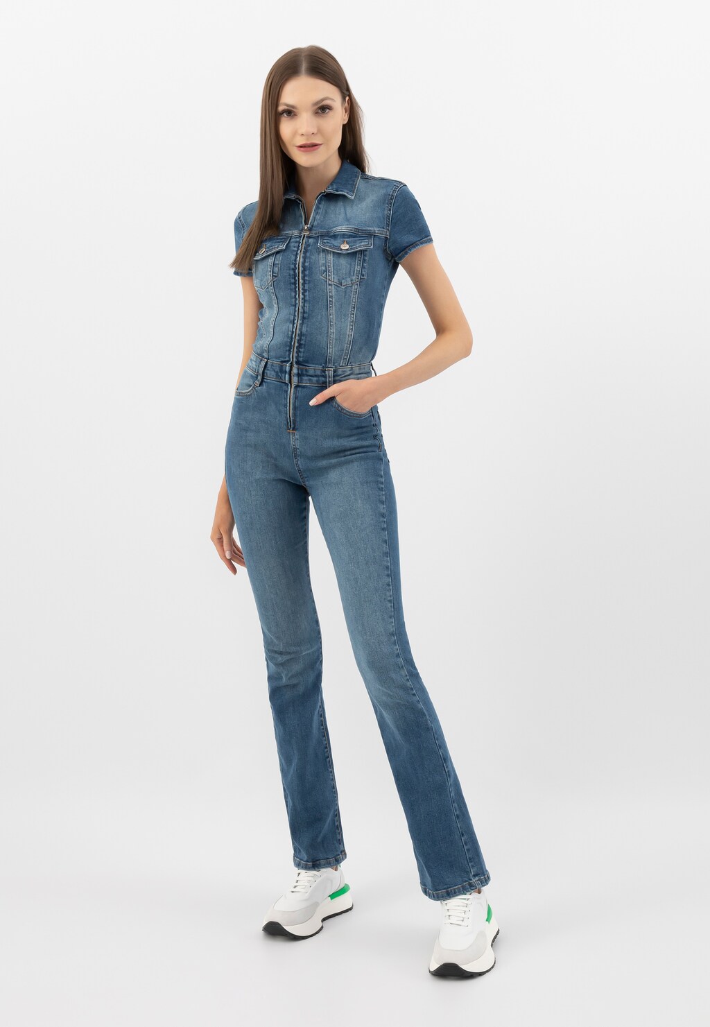 Modelka w jeansowym kombinezonie prezentuje białe sneakersy damskie Wojas model 46288-79 z charakterystycznymi zielonymi akcentami. Stylizacja na co dzień.