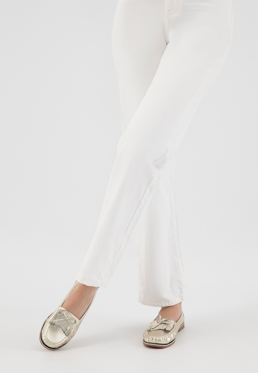 Złote mokasyny Wojas model 46293-58 z frędzlami i kokardką na gumowej podeszwie, przedstawione na nogach ubranych w białe spodnie.