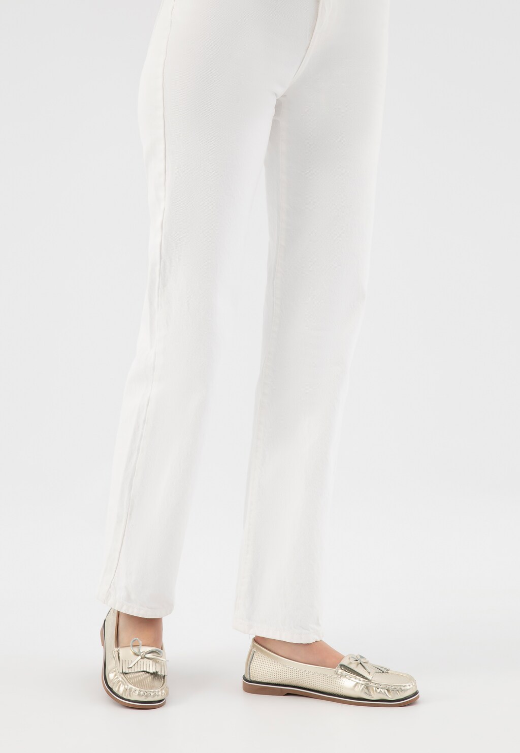 Eleganckie złote mokasyny Wojas model 46293-58 z ozdobnym frędzlem i perforacją, na płaskiej gumowej podeszwie, stylizowane na białych spodniach.