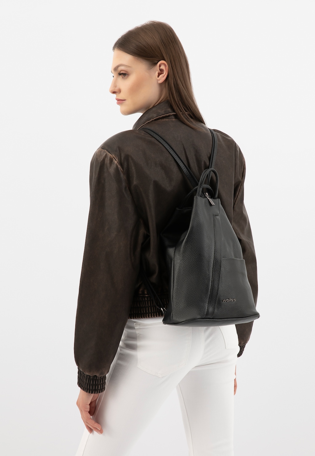 Czarny plecak Wojas model 80083-51 ze skóry licowej noszony na plecach, widoczny z profilu. Eleganckie połączenie z ciemną kurtką i białymi spodniami.