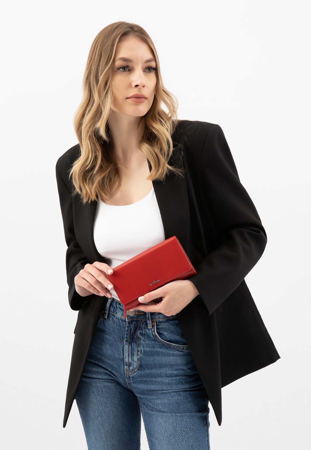 Elegancki czerwony portfel damski Wojas 91069-55 ze skóry licowej trzymany w dłoni. Stylowa kompozycja z czarną marynarką, białym topem i jeansami.