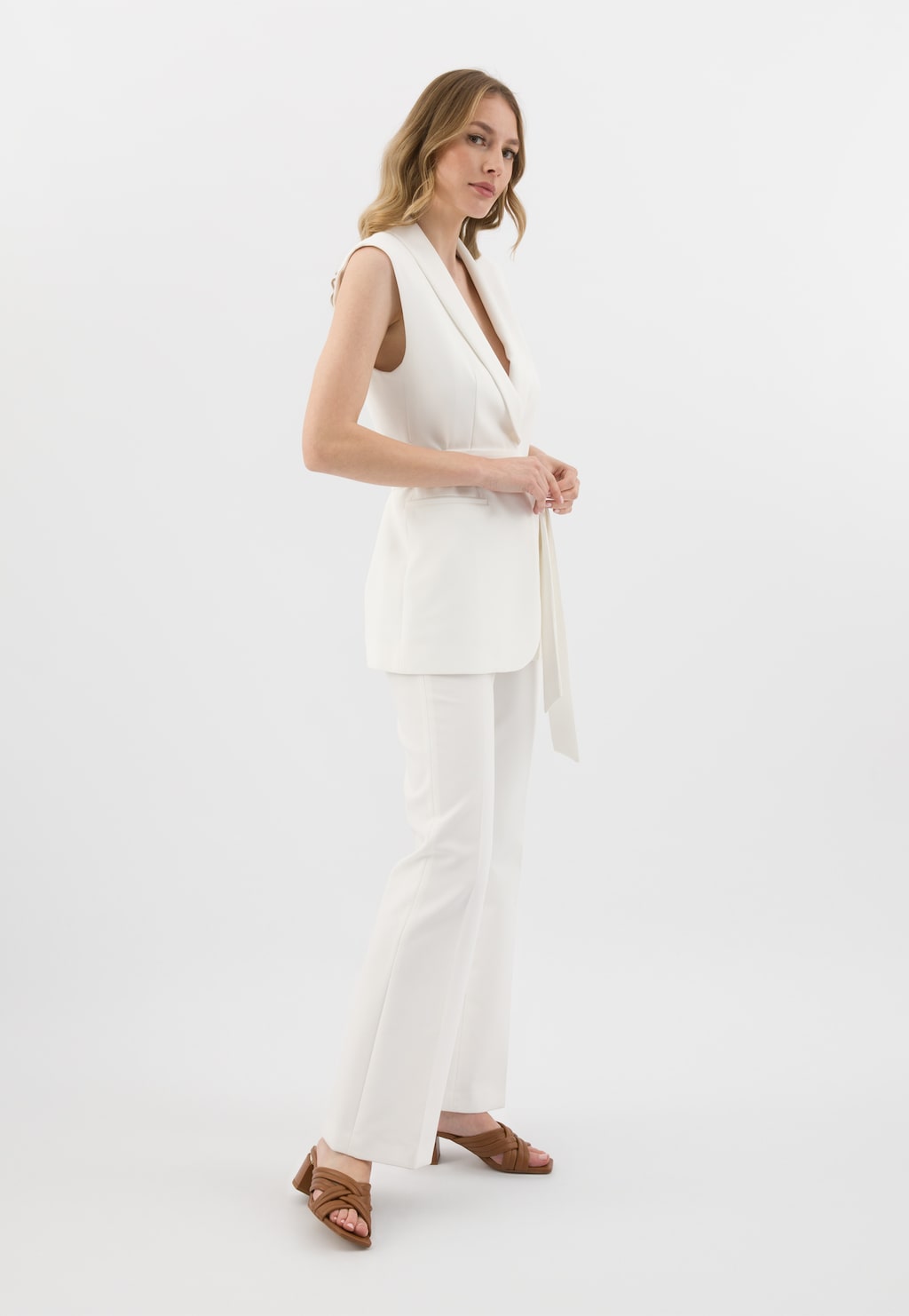 Jasnobrązowe klapki Wojas 74072-54 na obcasie z przeplatanymi paskami prezentowane na modelce w eleganckim białym garniturze, ukazujące stylową kombinację obuwia z formalnym strojem.