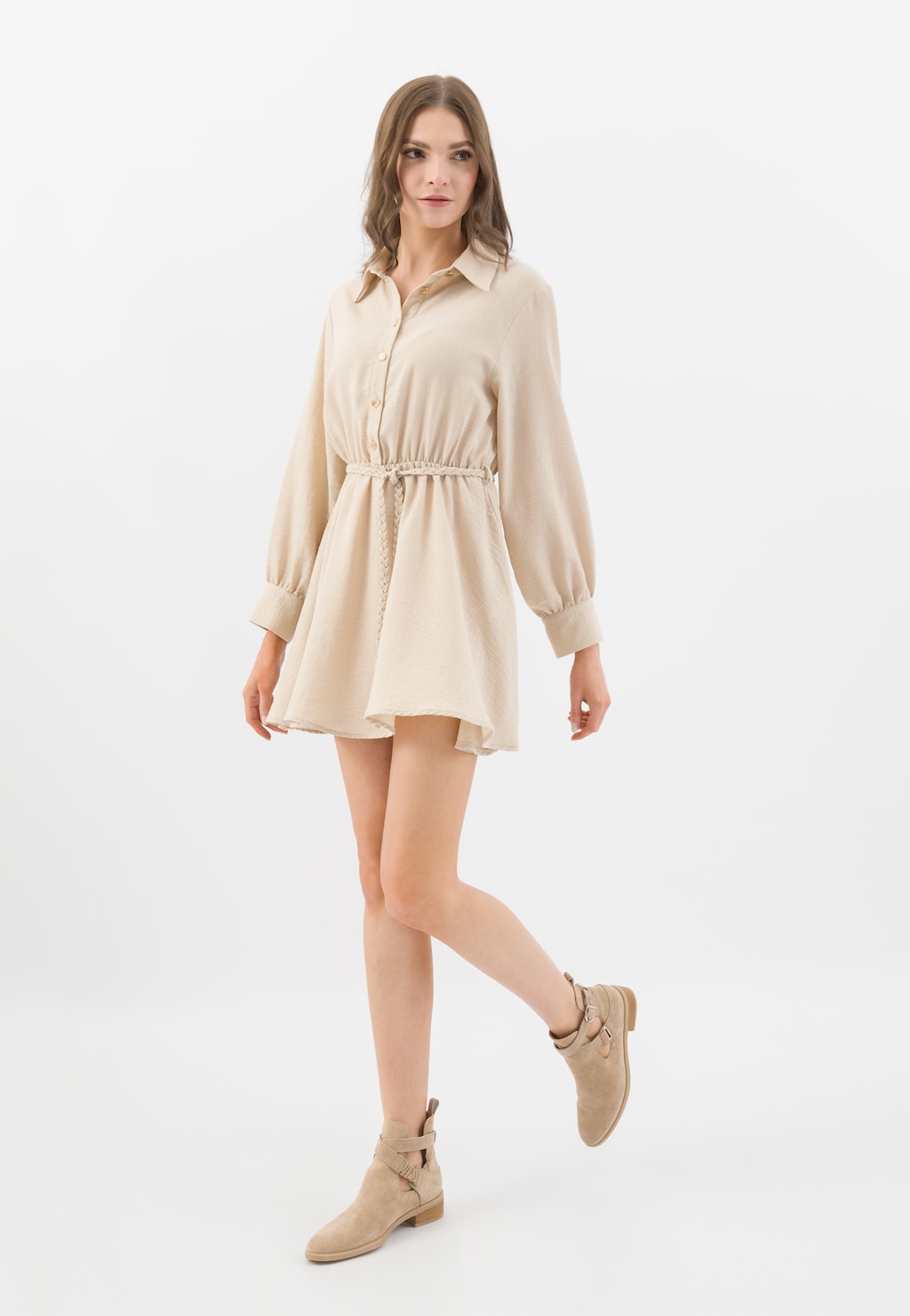 Modelka w beżowej sukience koszulowej prezentująca beżowe botki Wojas z wycięciami model 55248-64, widoczne z boku, z paskami przy kostce, dopasowane do całej stylizacji.