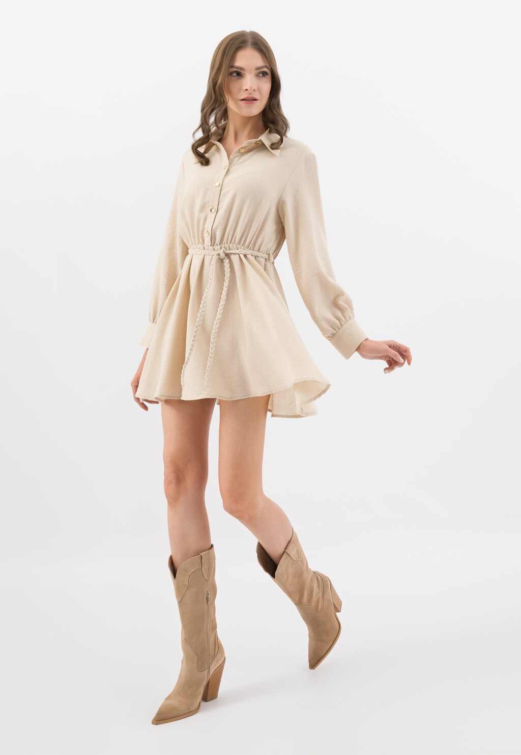 Modelka w beżowej sukience typu koszulowego prezentuje kozaki kowbojki Wojas model 71055-64 w beżowym kolorze na wysokim obcasie, ukazując ich stylowy wygląd i dopasowanie.