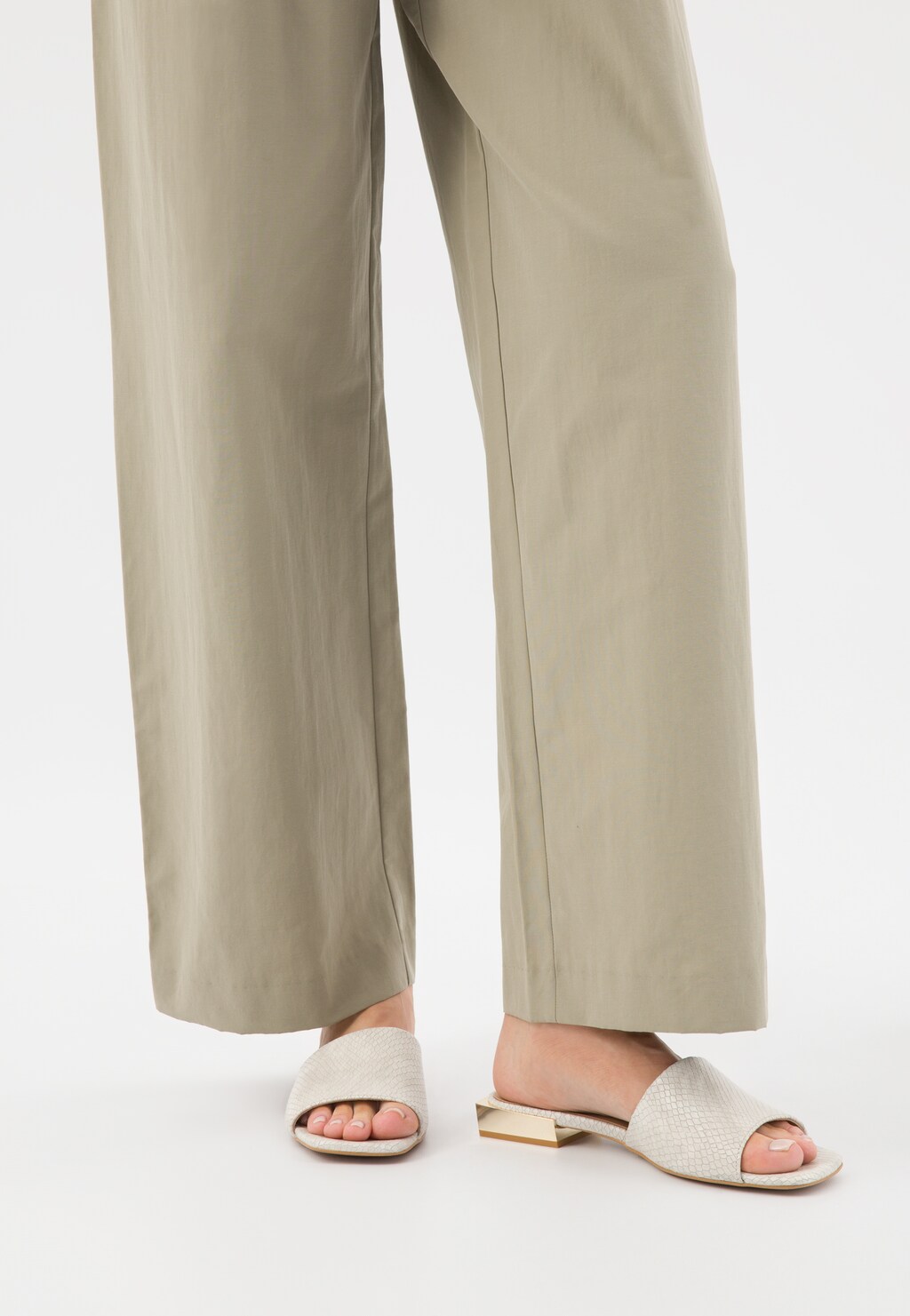 Beżowe klapki Wojas z tłoczoną skórą model 74122-54 ze złotym obcasem na nogach osoby w szerokich beżowych spodniach. Widoczna elegancka stylistyka butów.