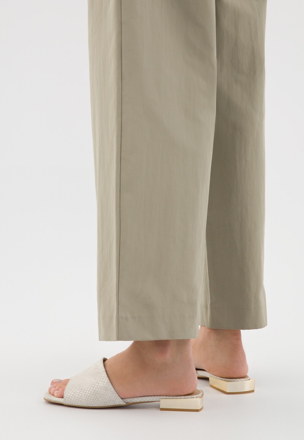Beżowe klapki Wojas model 74122-54 z tłoczoną skórą i złotym obcasem, prezentowane na nogach osoby w beżowych szerokich spodniach. Widok z boku.