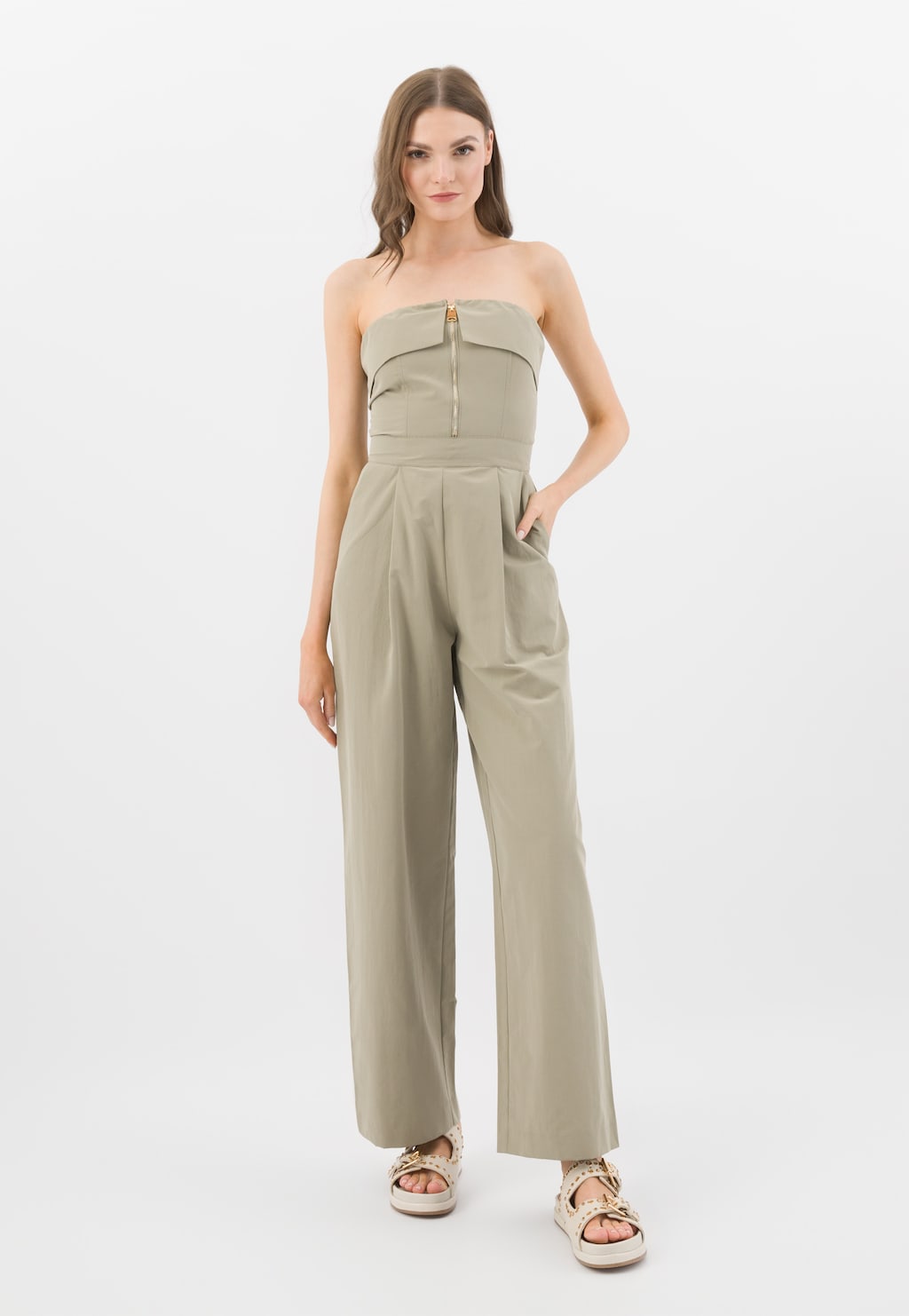 Kobieta w beżowym kombinezonie prezentująca płaskie skórzane klapki Wojas model 74125-54 w kolorze beżowym ze złotymi nitami.