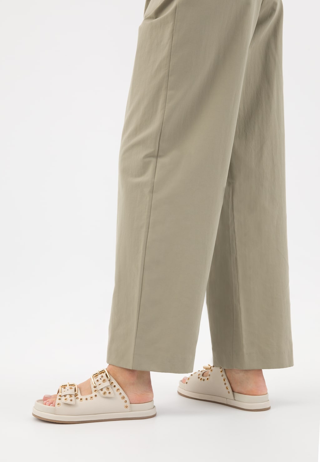 Beżowe skórzane klapki Wojas 74125-54 ze złotymi nitami, noszone z szerokimi beżowymi spodniami. Widok z boku pokazuje płaską podeszwę i dwupasmowy design klapków.