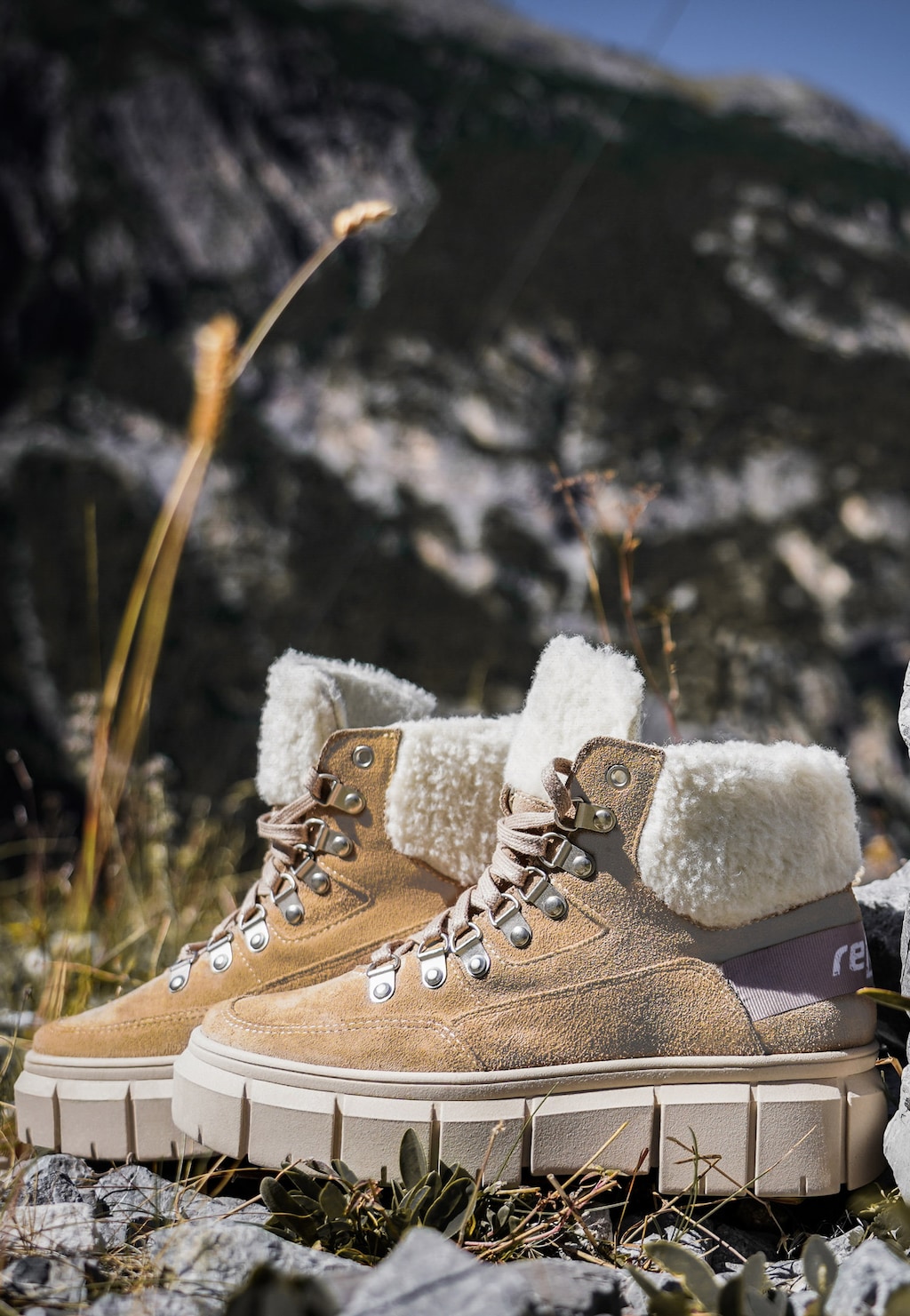 Beżowe trzewiki damskie RELAKS R64003-64 z białym kożuszkiem sfotografowane w górskim krajobrazie wśród skał, z górskimi szczytami w tle.