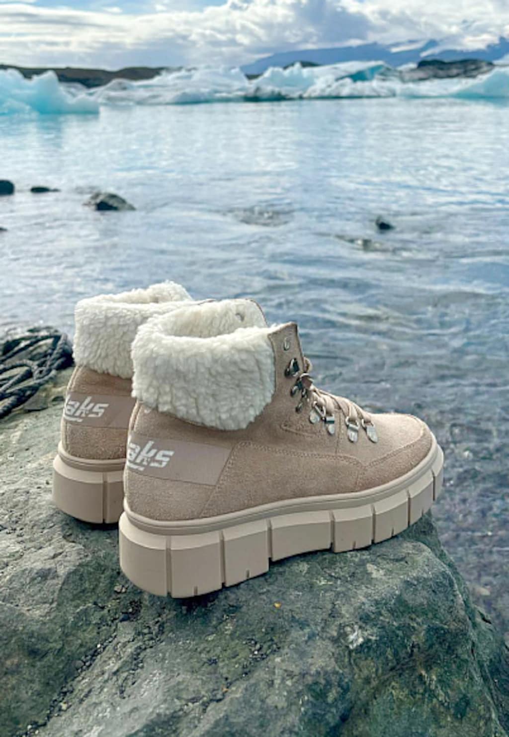 Beżowe trzewiki damskie RELAKS R64003-64 z białym kożuszkiem na kamienistym brzegu lodowatego jeziora z górami lodowymi w tle. Buty na platformie z wiązaniem.