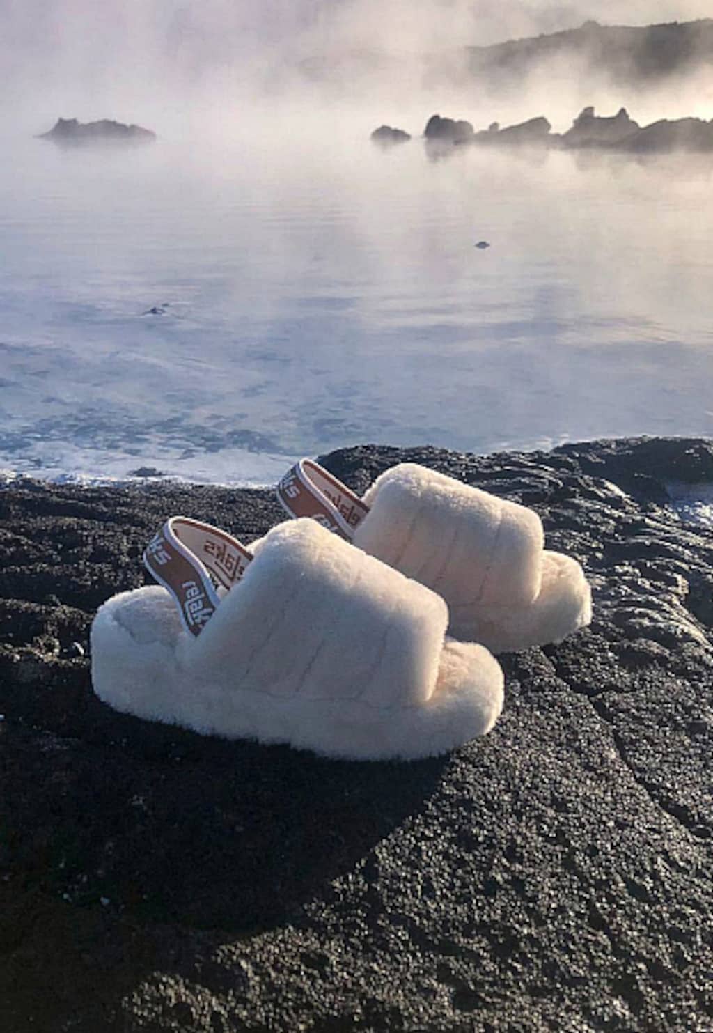 Beżowe puchate kapcie damskie Relaks R34006-64 z gumką sfotografowane na skałach nad wodą - puszyste obuwie domowe w naturalnym otoczeniu.