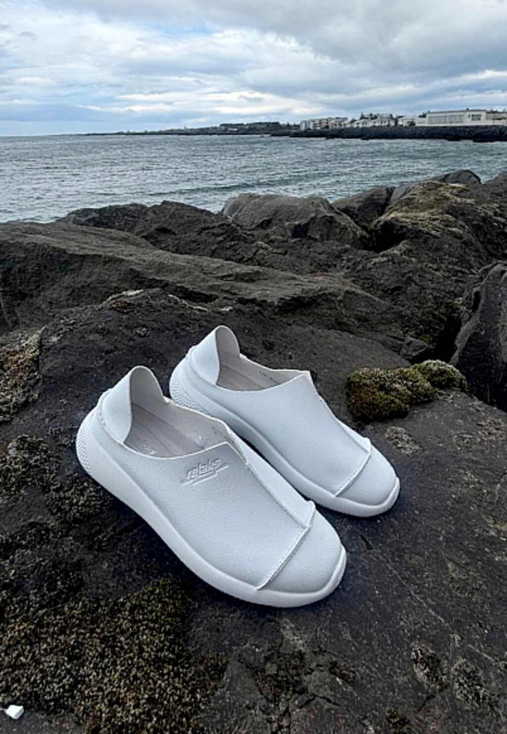 Lekkie białe półbuty RELAKS model R46168-19 sfotografowane na skałach nad wodą. Eleganckie, wsuwane buty o minimalistycznym designie, idealne na ciepłe dni.