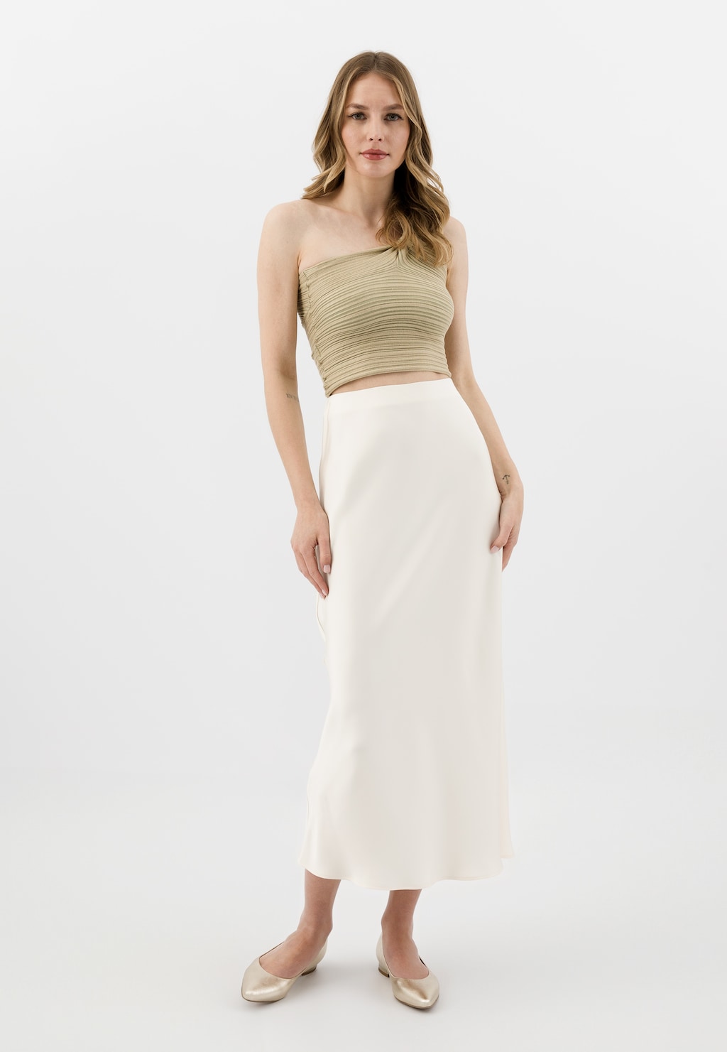 Modelka w beżowym topie i białej długiej spódnicy, prezentująca złote baleriny damskie Wojas model 44033-58 na niskim obcasie, idealne do eleganckich stylizacji.