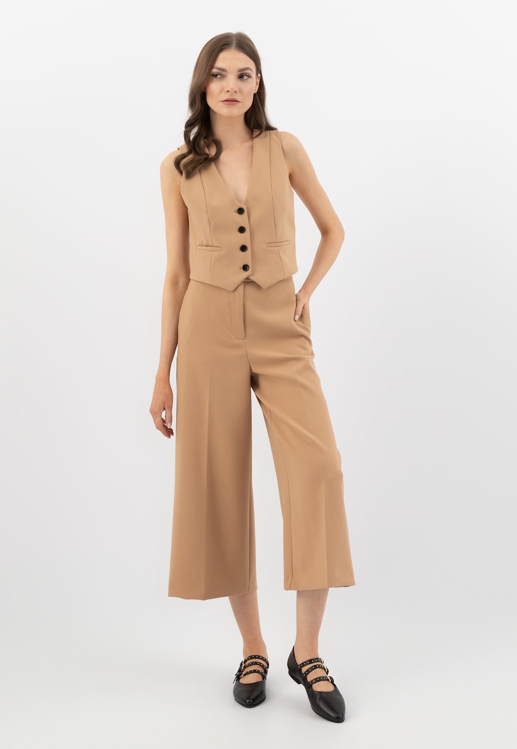 Modelka w beżowym komplecie z kamizelki i szerokich spodni, prezentująca baleriny Wojas model 44042-51 w stylu Mary Jane z trzema paskami w kolorze czarnym.