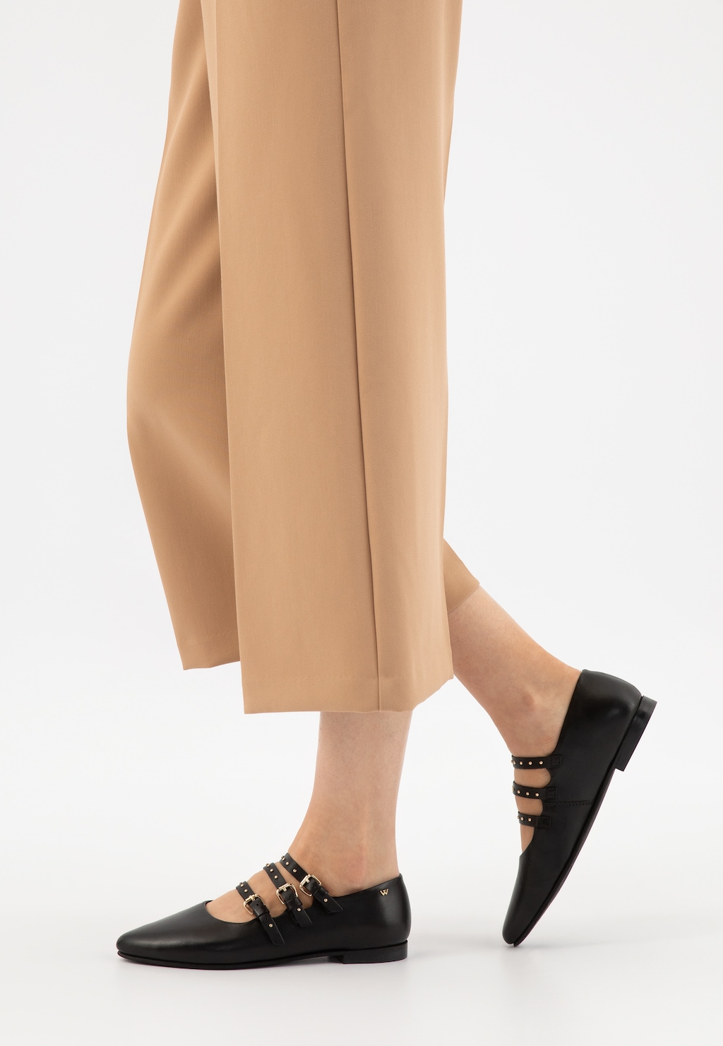 Czarne baleriny Wojas model 44042-51 w stylu Mary Jane z trzema paskami na stopie kobiety ubranej w beżowe spodnie. Widok z boku ukazujący eleganckie wykończenie buta.