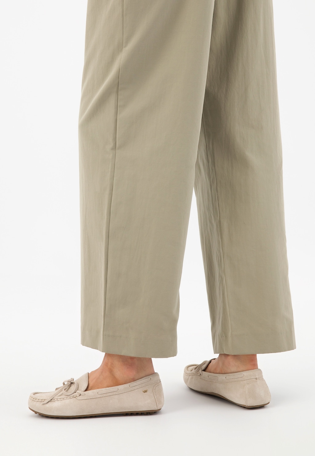 Beżowe mokasyny damskie Wojas model 46270-64 z wypustkami na podeszwie, widoczne na nogach osoby w jasnych, szerokich spodniach. Eleganckie buty z ozdobnym wiązaniem.