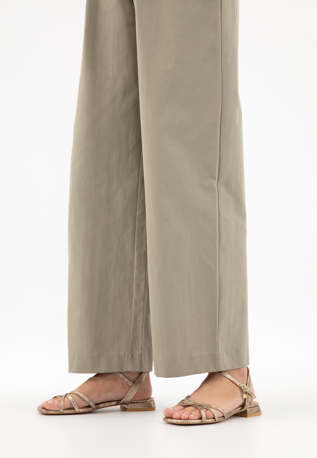 Eleganckie złote sandały Wojas model 76171-58 wykonane z tłoczonej skóry, ukazane na nogach osoby noszącej beżowe szerokie spodnie. Sandały mają cienkie paski i niski obcas.
