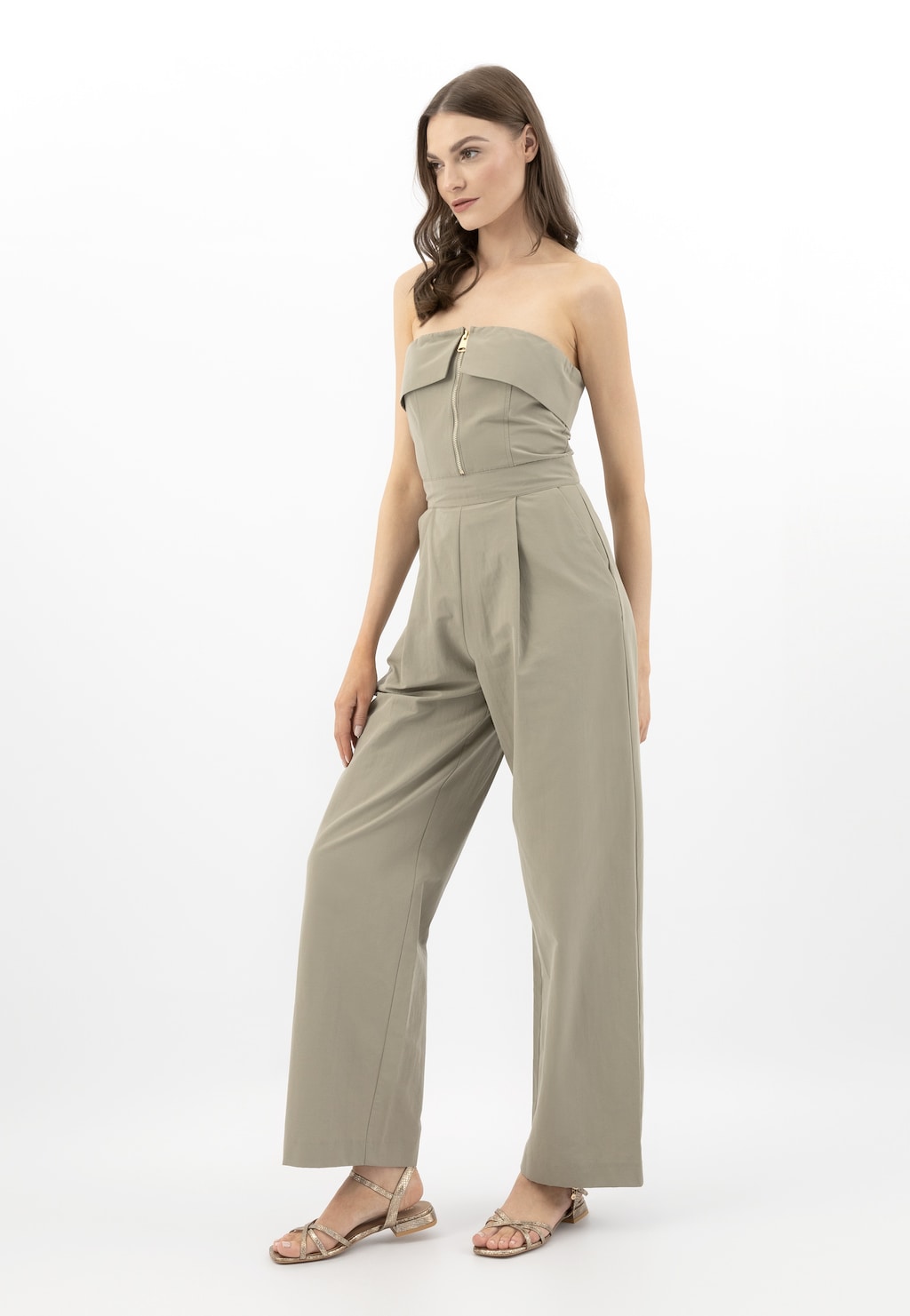 Modelka w beżowym kombinezonie prezentuje złote sandały Wojas model 76171-58 z tłoczonej skóry. Eleganckie płaskie obuwie z paskami na kostce współgra ze stylizacją.