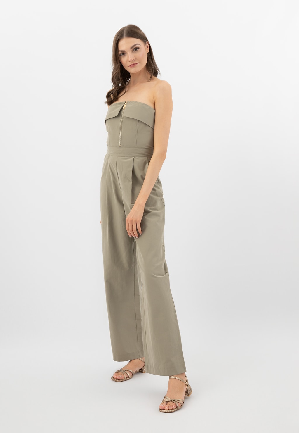 Modelka w beżowym kombinezonie bez ramiączek, prezentująca złote sandały Wojas model 76171-58 z tłoczonej skóry, widoczne na stopach.