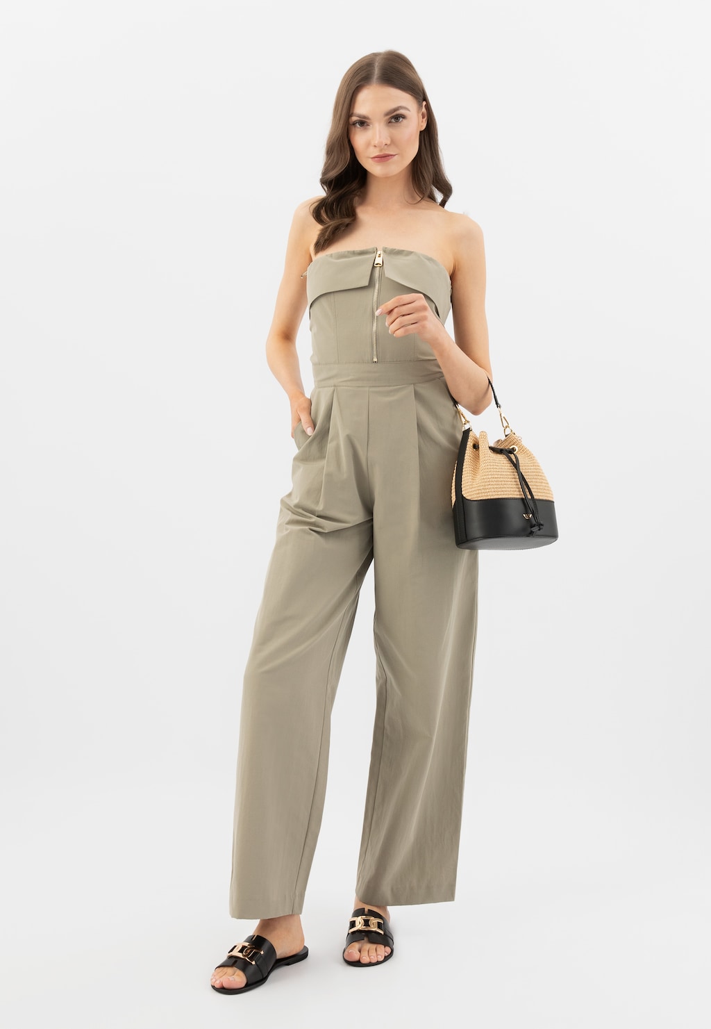 Modelka w beżowym kombinezonie trzyma beżowo-czarną torebkę Wojas 80378-81 ze skóry licowej i rafii. Elegancki strój uzupełniają czarne klapki.