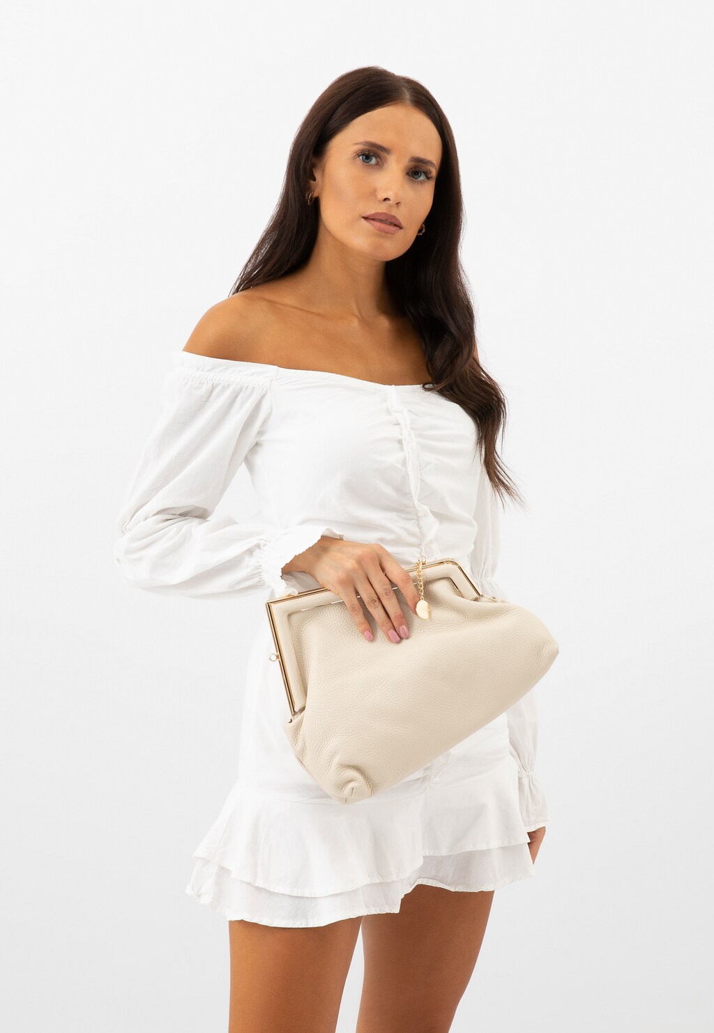 Modelka w białej sukience hiszpance prezentuje małą, asymetryczną torebkę damską Wojas 80390-54 w jasnym beżu z eleganckim złotym zapięciem.