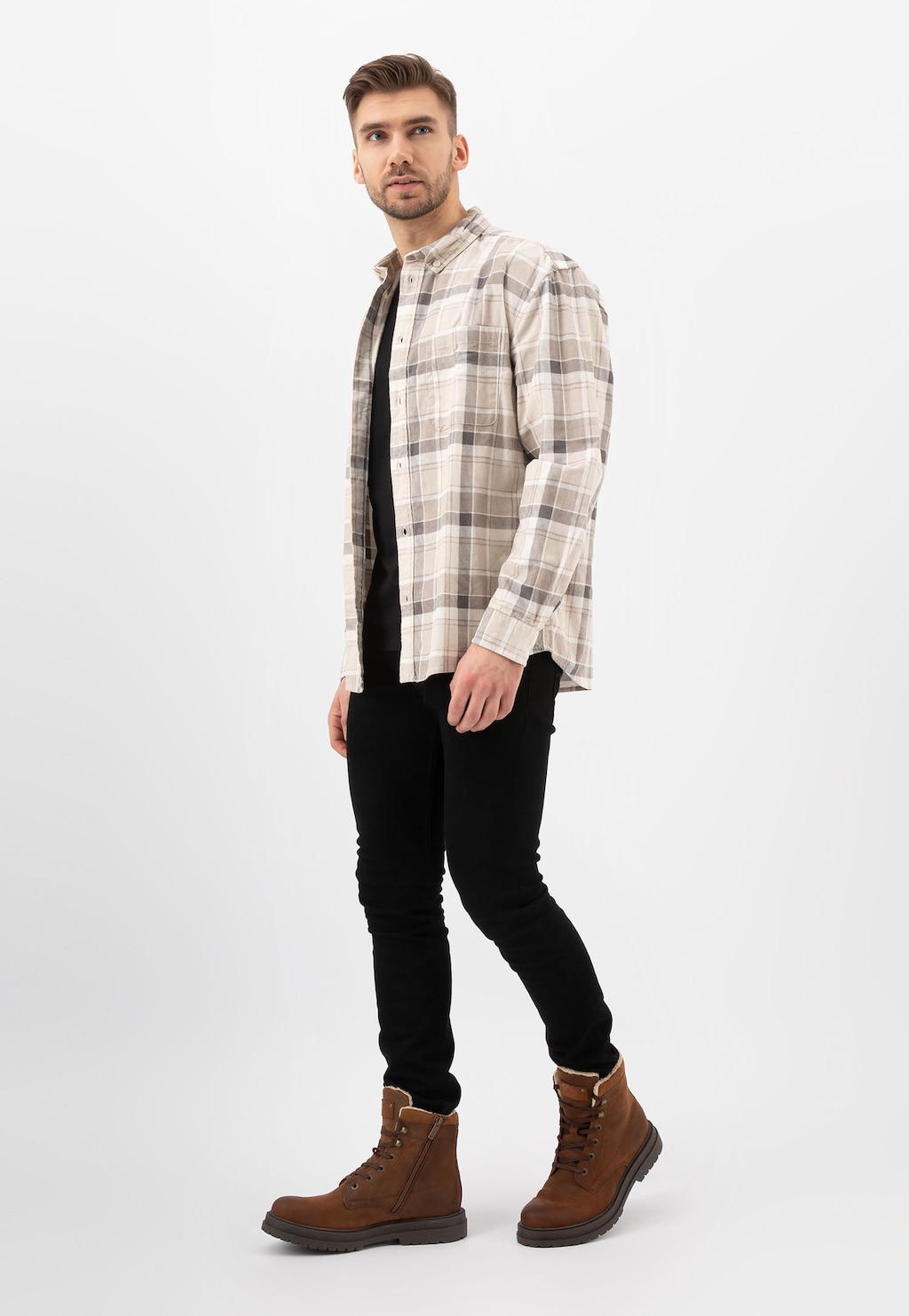 Model prezentuje brązowe męskie trzewiki Wojas 24077-93 typu bikery z ociepleniem, nosząc kraciastą koszulę i czarne spodnie. Buty mają klasyczny fason i praktyczne zapięcie na suwak.