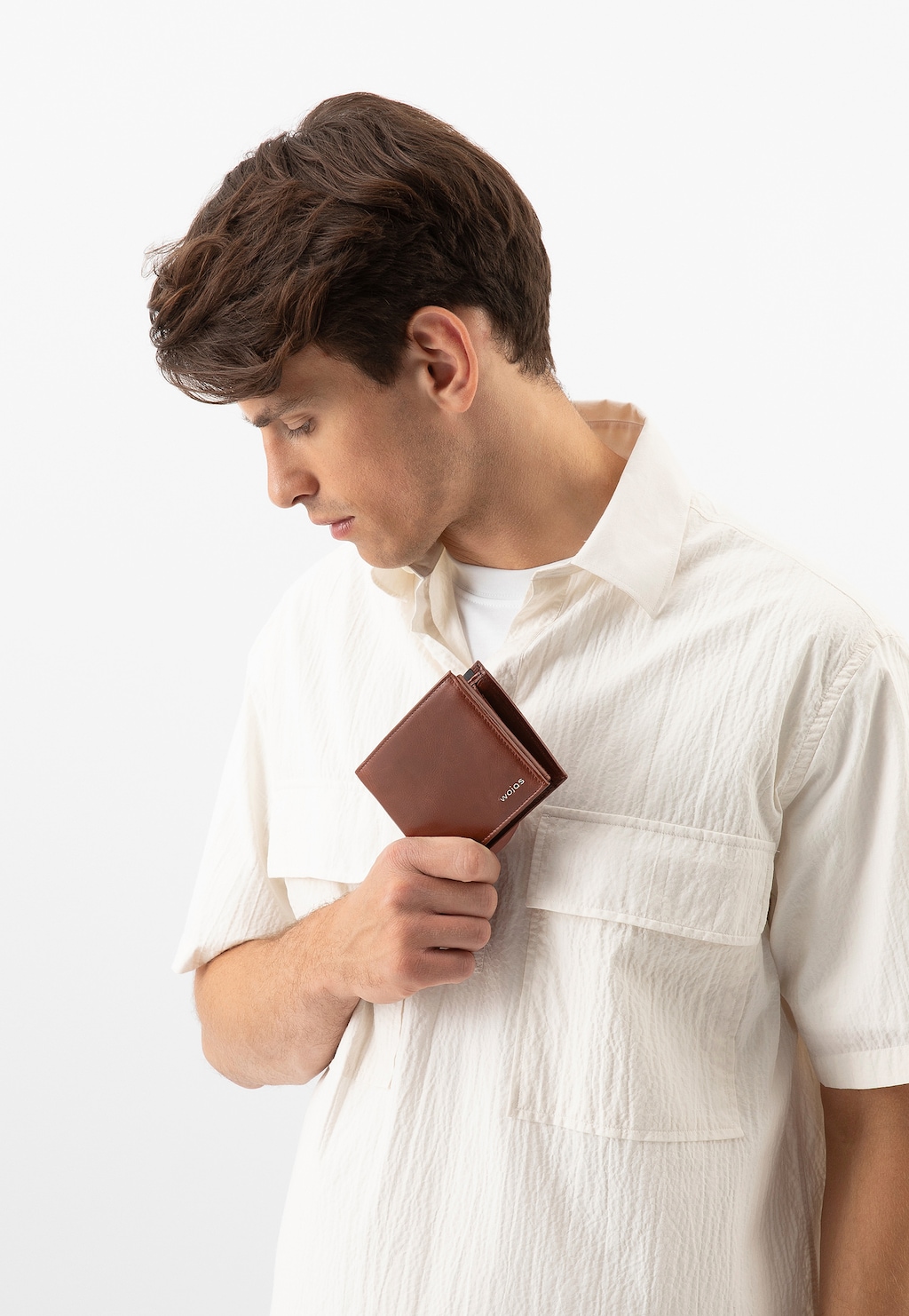 Mężczyzna w białej koszuli trzymający brązowy skórzany portfel Wojas model 8938-53 z ochroną RFID. Elegancki dodatek pokazany z profilu w minimalistycznej stylizacji.