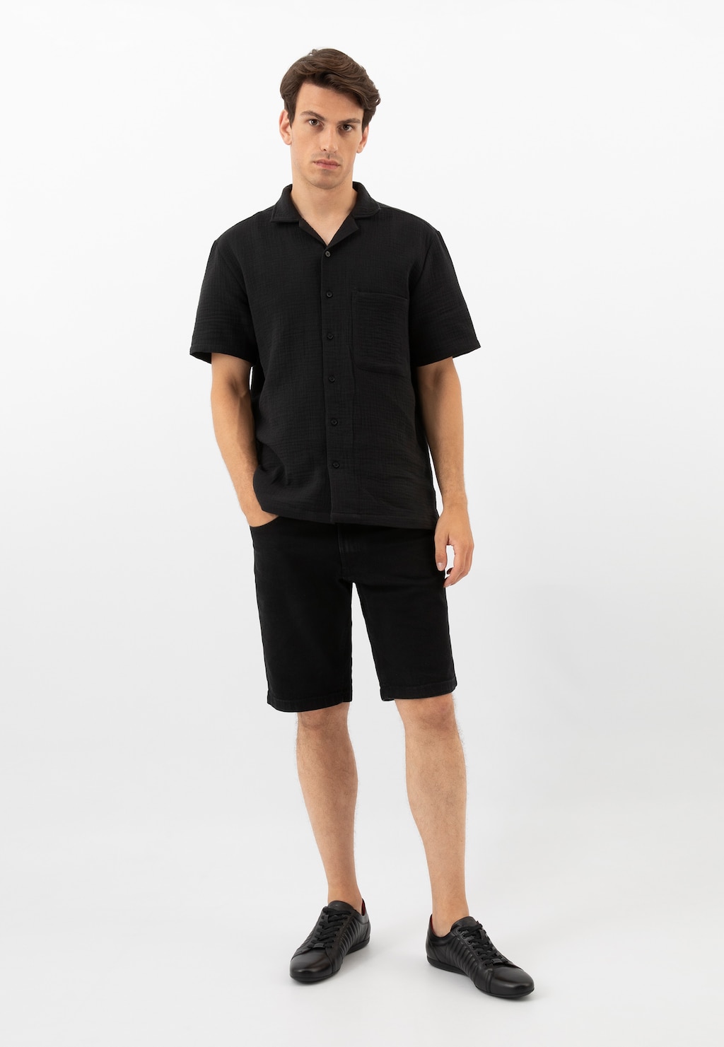 Model ubrany w czarną koszulę i szorty prezentuje eleganckie czarne półbuty Wojas model 9012-51, idealne do letnich stylizacji.