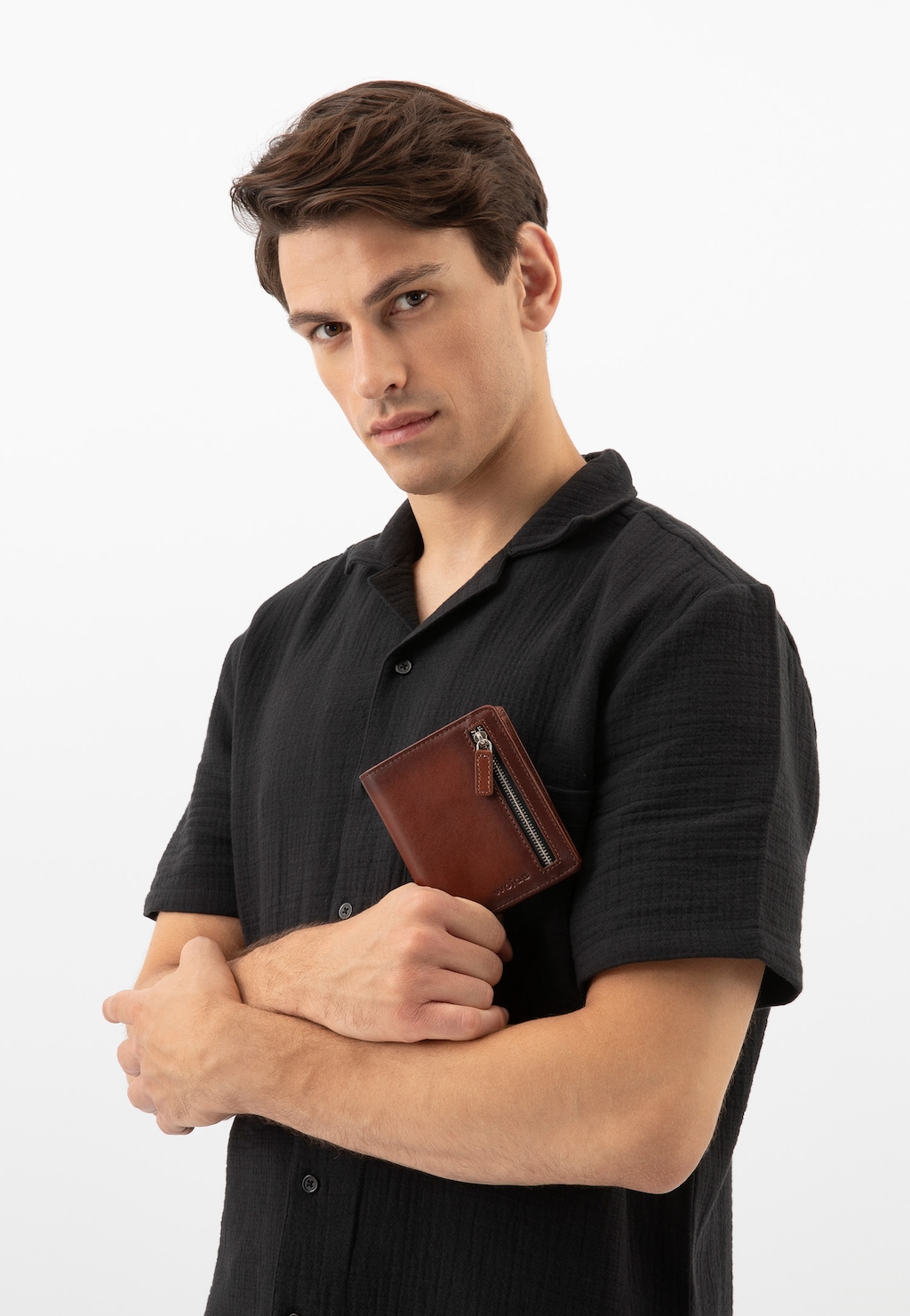 Elegancki brązowy portfel męski Wojas model 9959-52 trzymany przez osobę w czarnej koszuli. Widoczne zapięcie na zamek, wykonany z wysokiej jakości skóry.