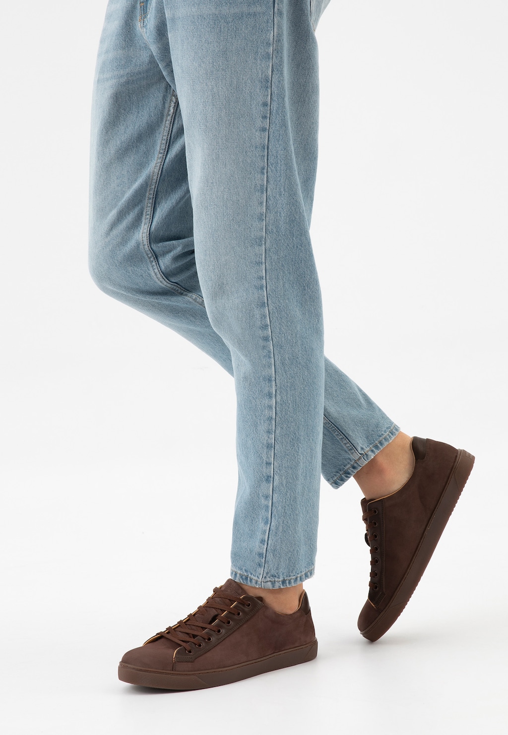 Ciemnobrązowe trampki męskie Wojas model 10227-72 ze skórzanymi wstawkami, noszone do jasnych jeansów. Buty prezentowane w widoku bocznym na nodze.