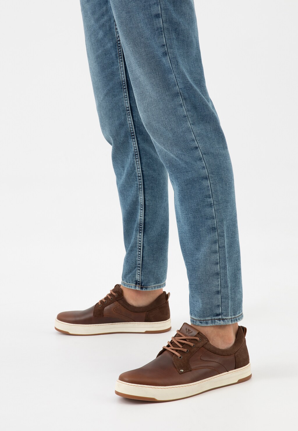 Brązowe trampki Wojas model 10220-72 z łączonych skór na białej podeszwie prezentowane na nogach w jasnoniebieskich jeansach, widok z boku.