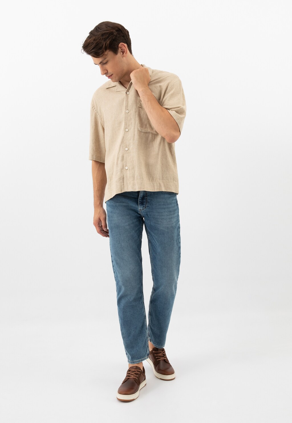 Model w beżowej koszuli i jeansach prezentuje brązowe trampki Wojas 10220-72 z łączonych skór na białej podeszwie, doskonałe do codziennych stylizacji.